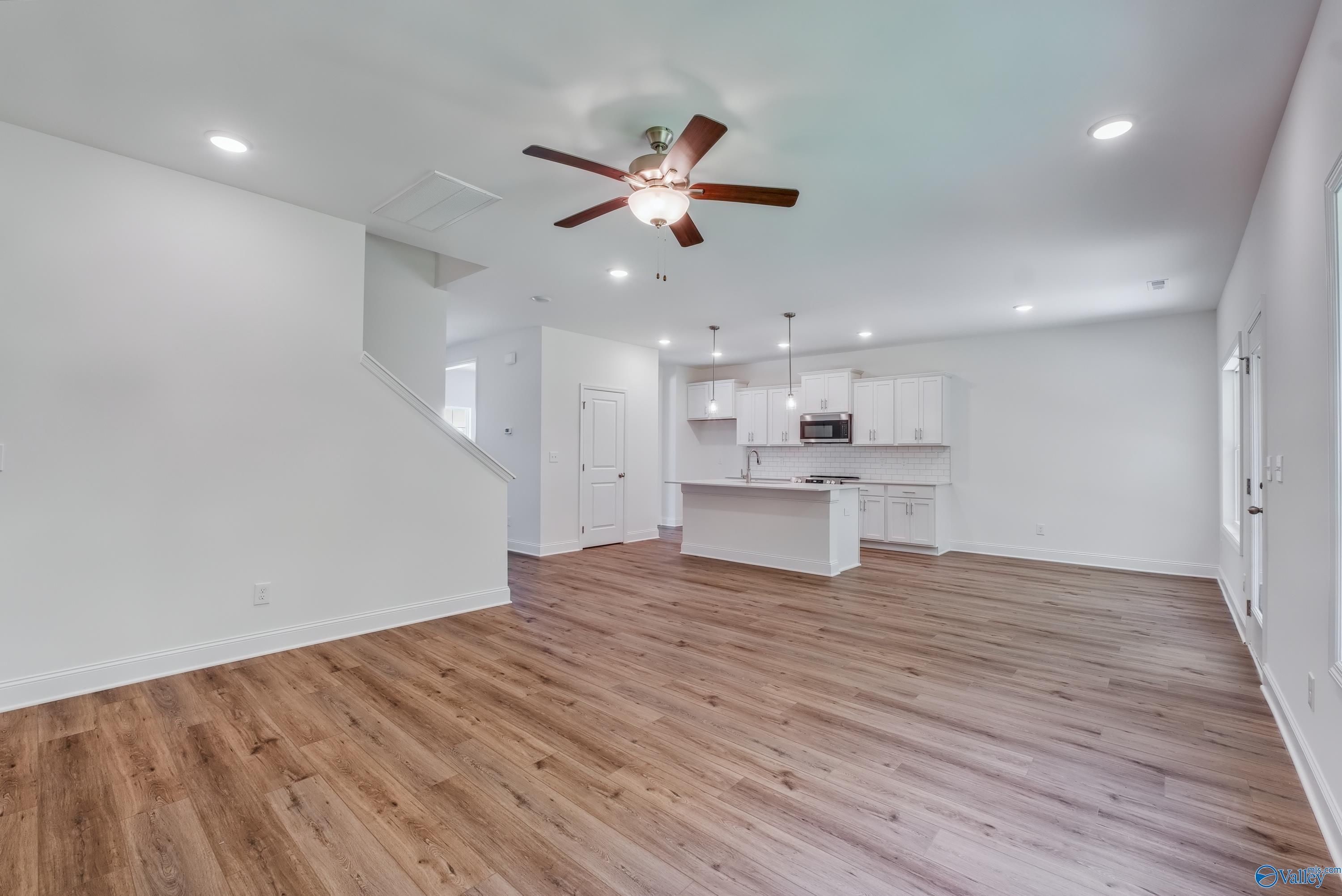 Open-concept living-kitchen with hardwood floors, white island cabinets, ceiling fan, stairs in Shelby A 4-bedroom home, Arab AL