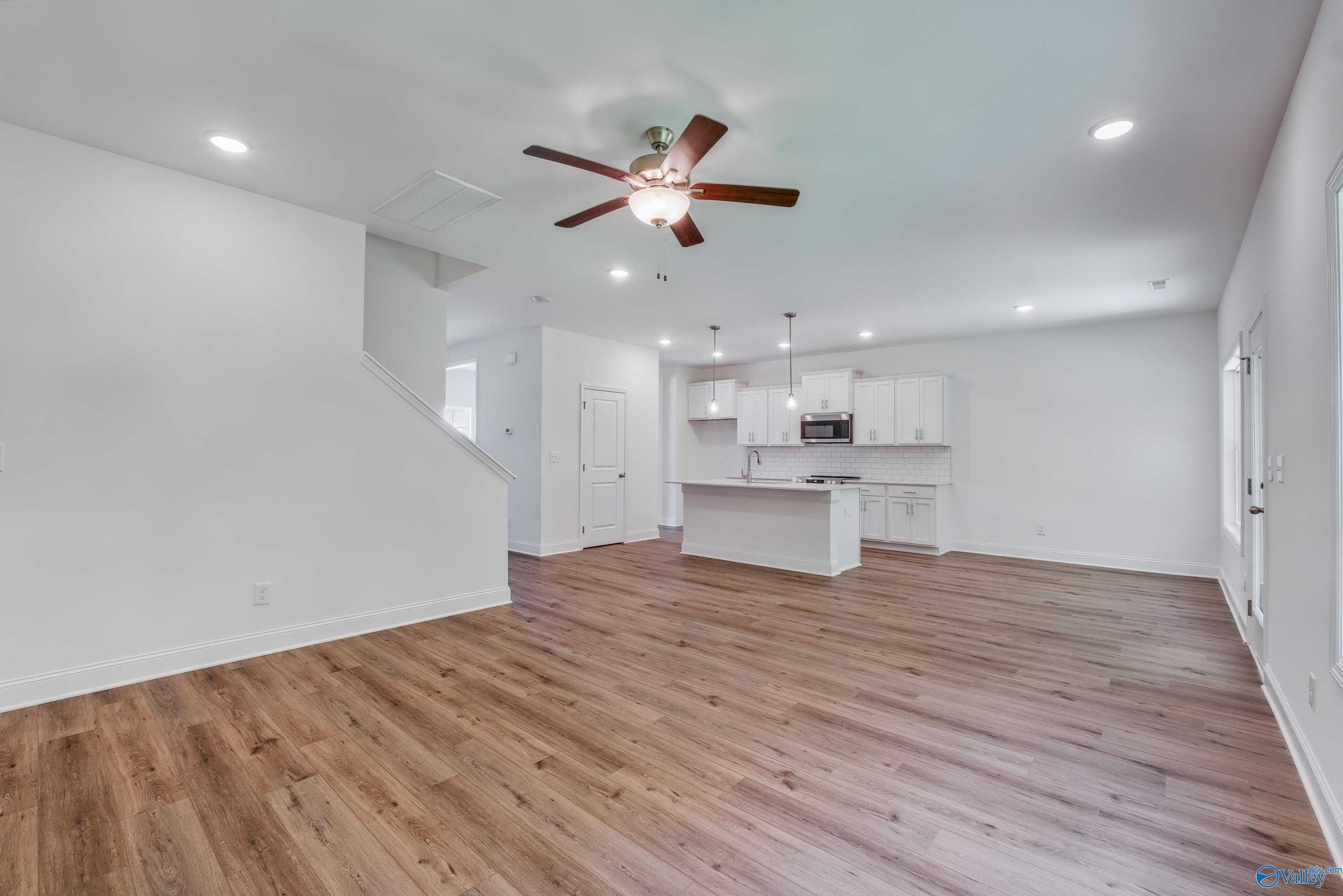 Open-concept living-kitchen with hardwood floors, white island cabinets, ceiling fan, stairs in Shelby A 4-bedroom home, Arab AL