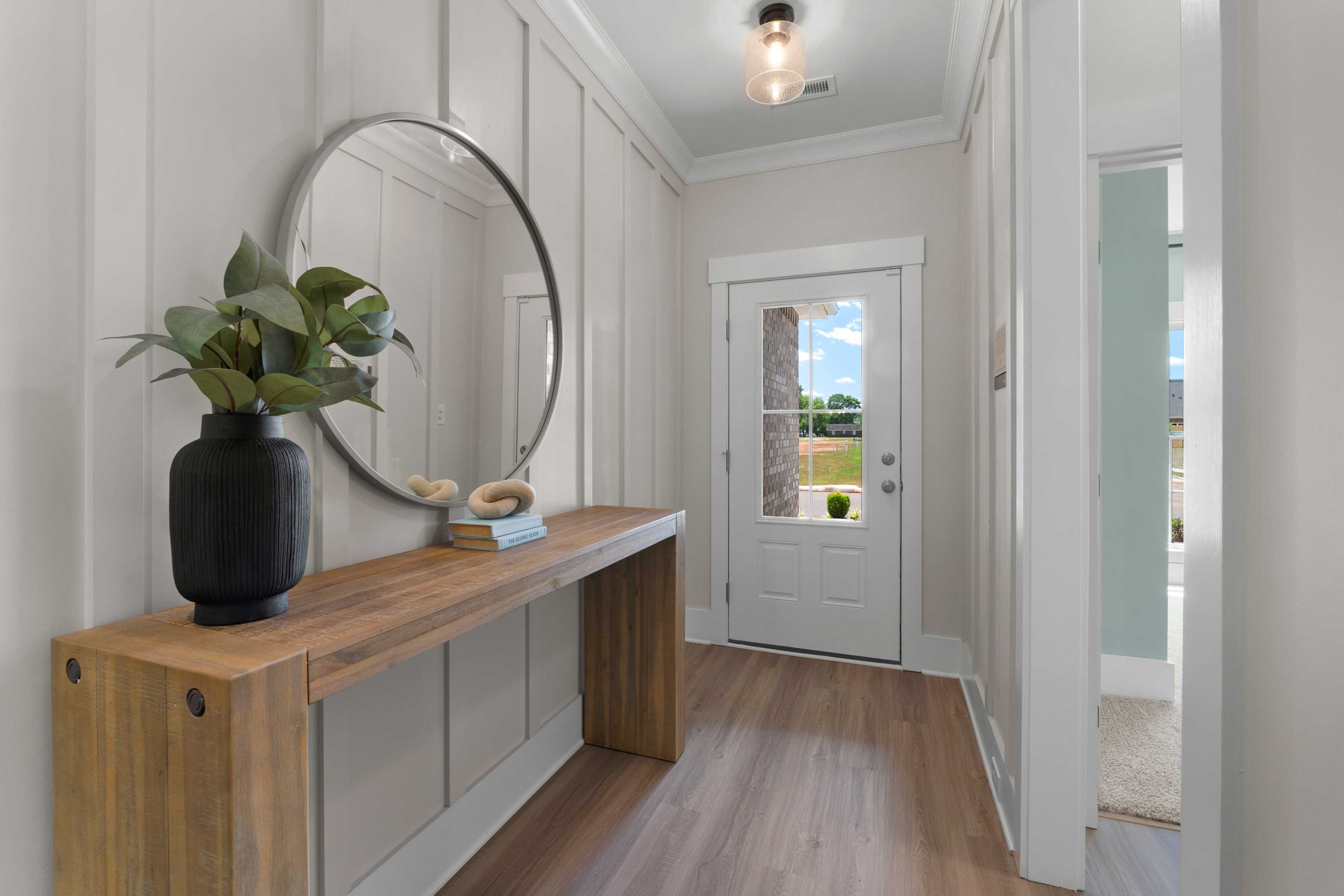Modern entryway foyer at Hollon Meadow in Decatur Alabama with wooden console table, round mirror, potted plant, and glass front door