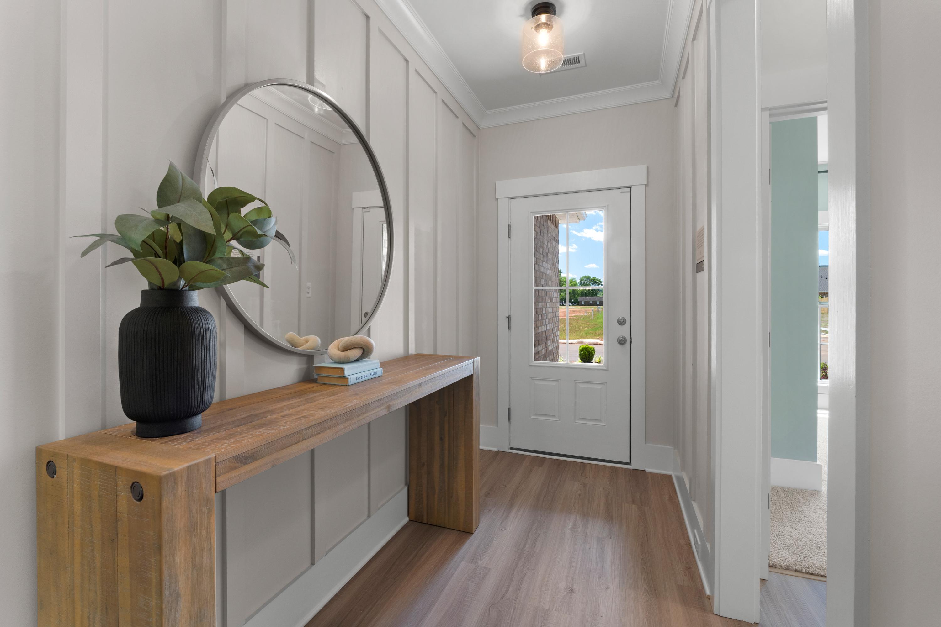 Modern entryway foyer at Hollon Meadow in Decatur Alabama with wooden console table, round mirror, potted plant, and glass front door