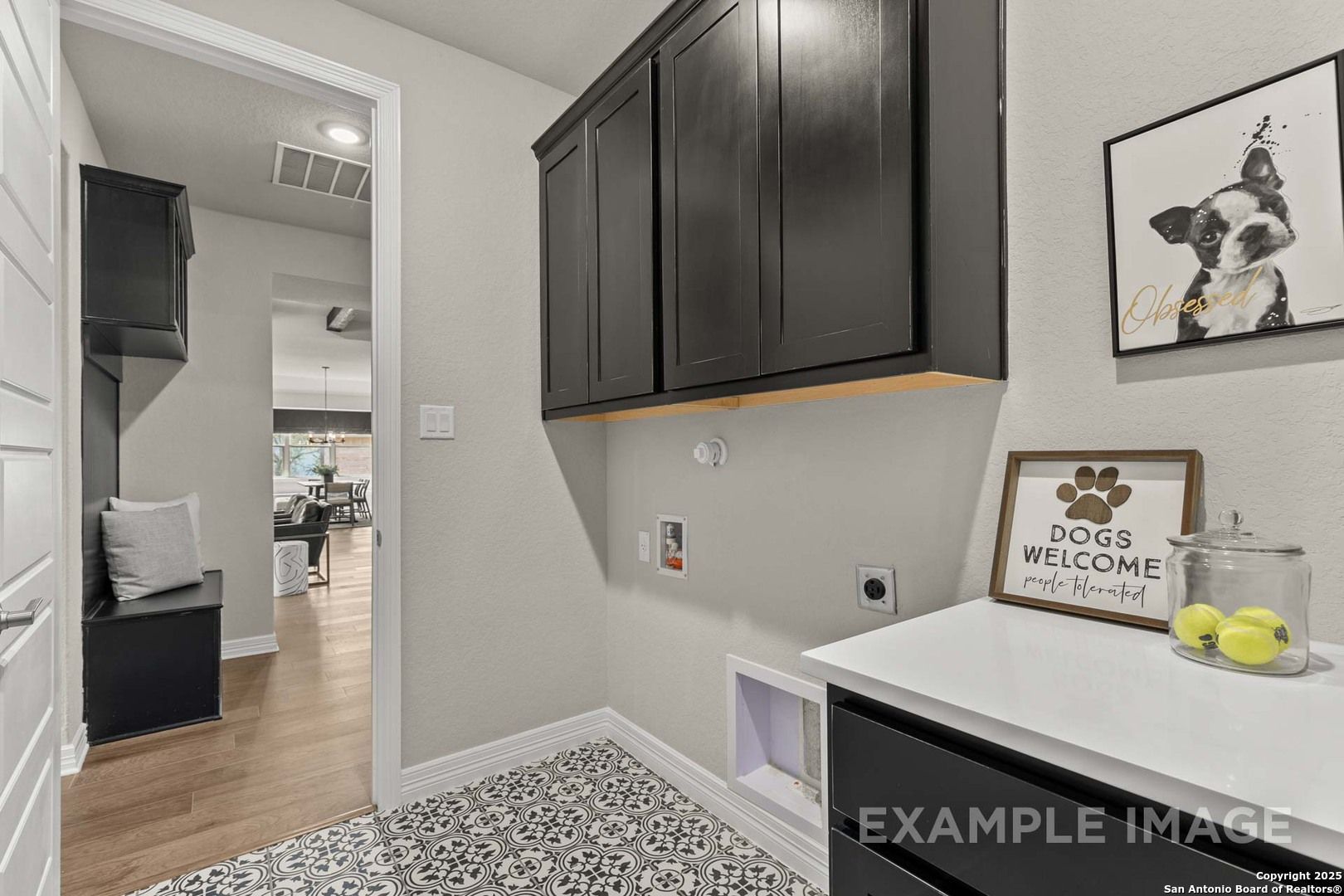 Pet-friendly laundry room with dark cabinets, white countertop, dog art, and welcome sign in The Summerlin B, Castroville, Texas