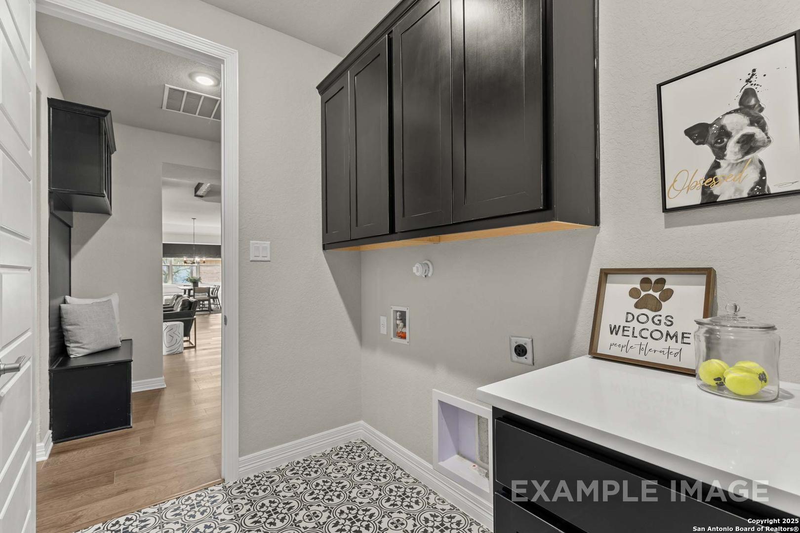 Pet-friendly laundry room with dark cabinets, white countertop, dog art, and welcome sign in The Summerlin B, Castroville, Texas