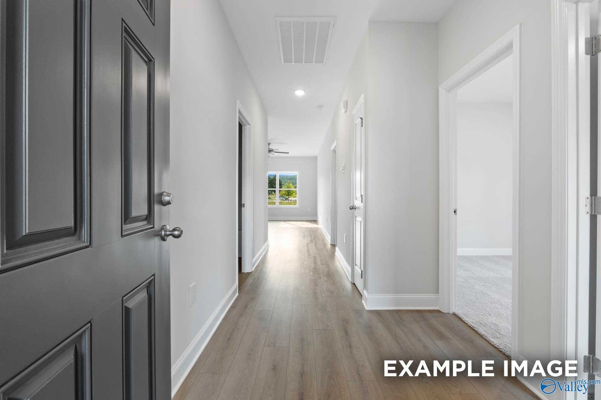 Bright entry hallway with light hardwood floors, white walls, and open gray door in Davidson Homes The Butler, Huntsville AL
