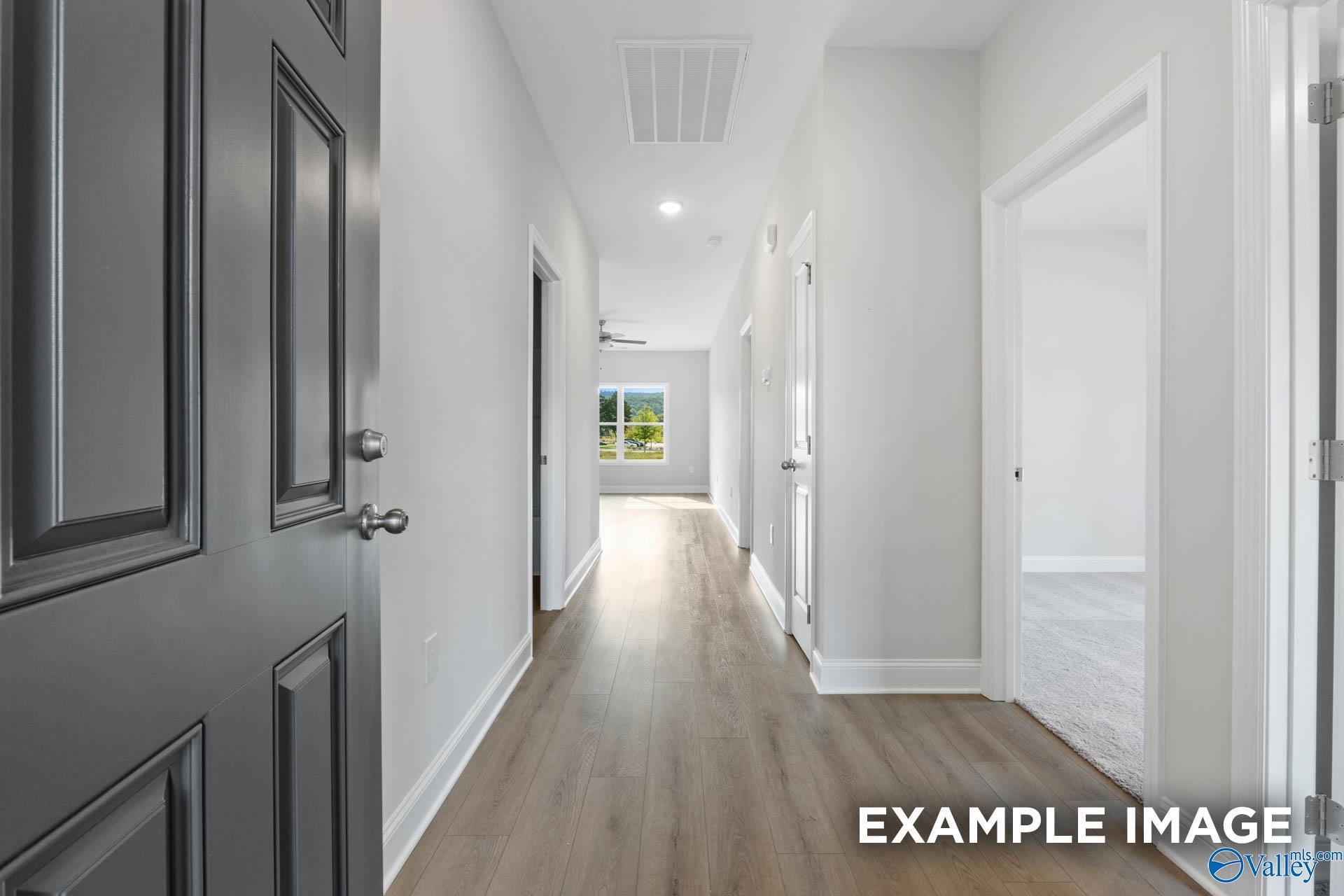 Bright entry hallway with gray front door, light wood floors, and white walls in Davidson Homes The Butler, Heritage Lakes, New Market, Alabama