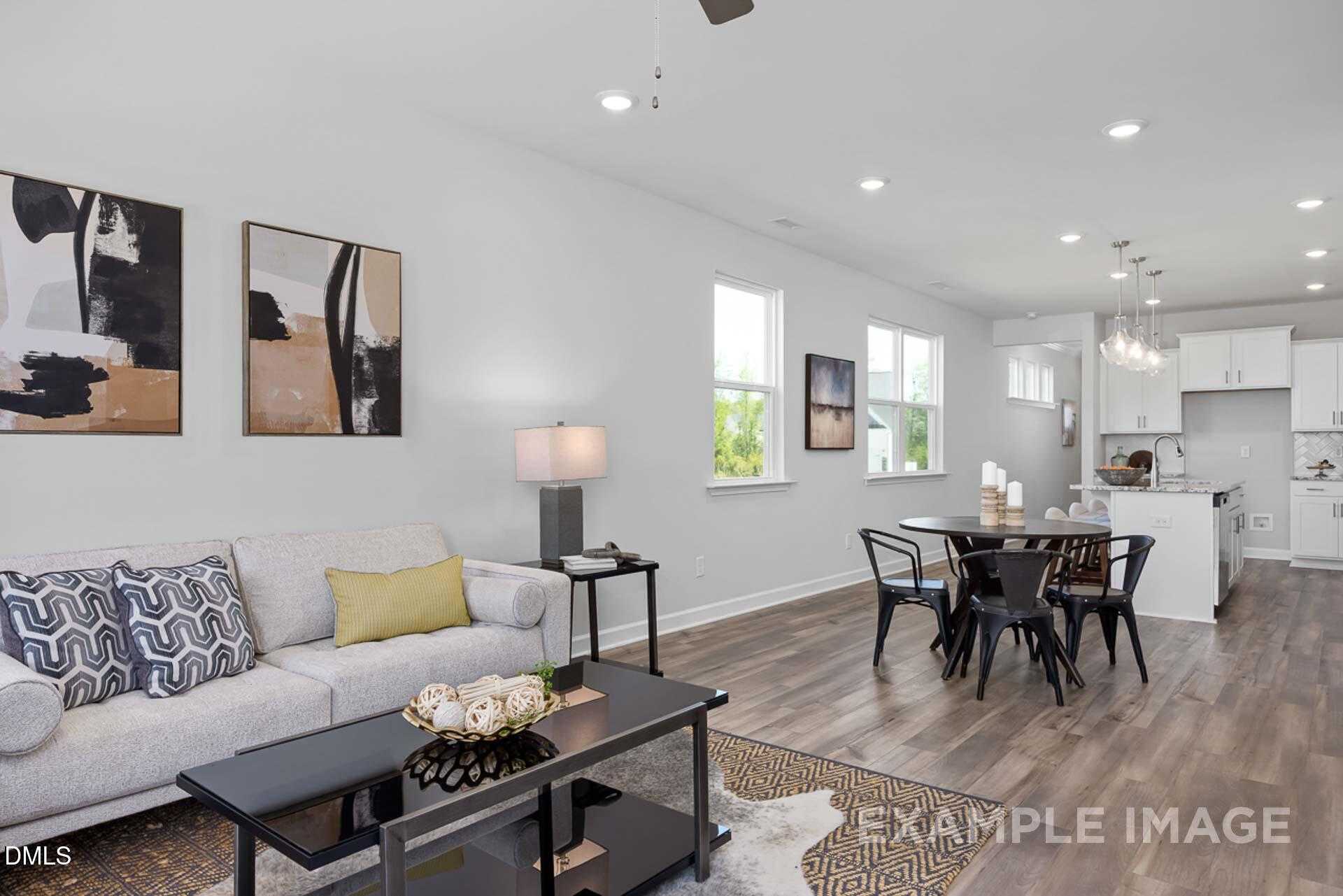 Open-concept living room with gray sofa, abstract art, dining table, and white kitchen in The Carter C by Davidson Homes, Lillington, NC