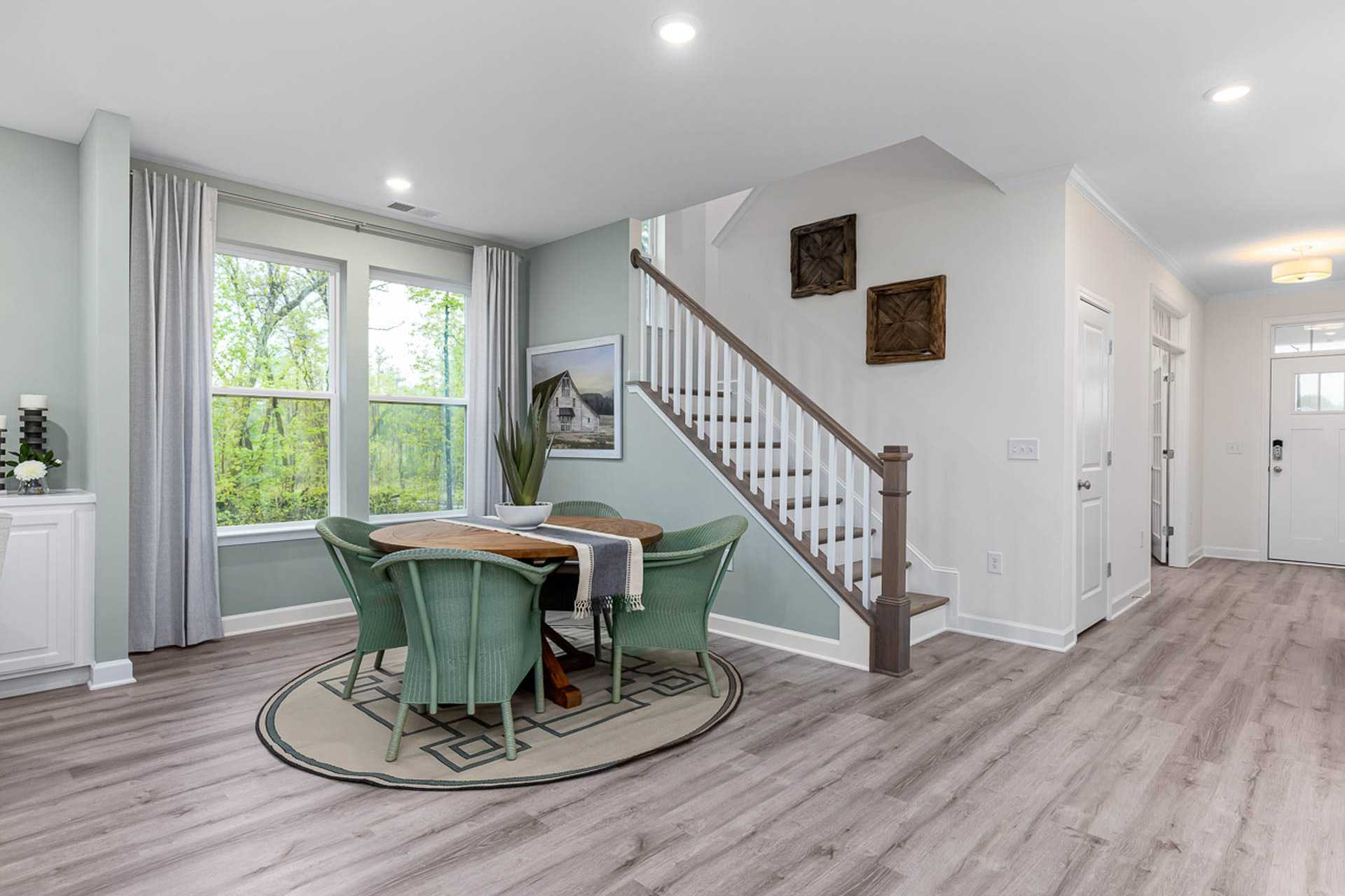 Open-concept dining area at Weatherford East in Angier NC with round green table, white staircase, and large windows