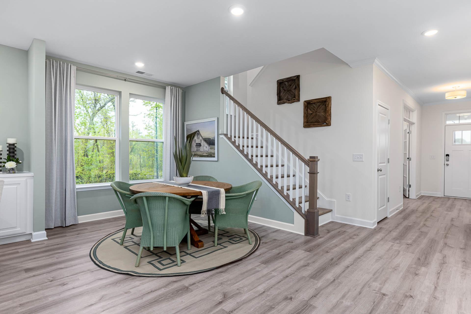 Open-concept dining area at Weatherford East in Angier NC with round green table, white staircase, and large windows