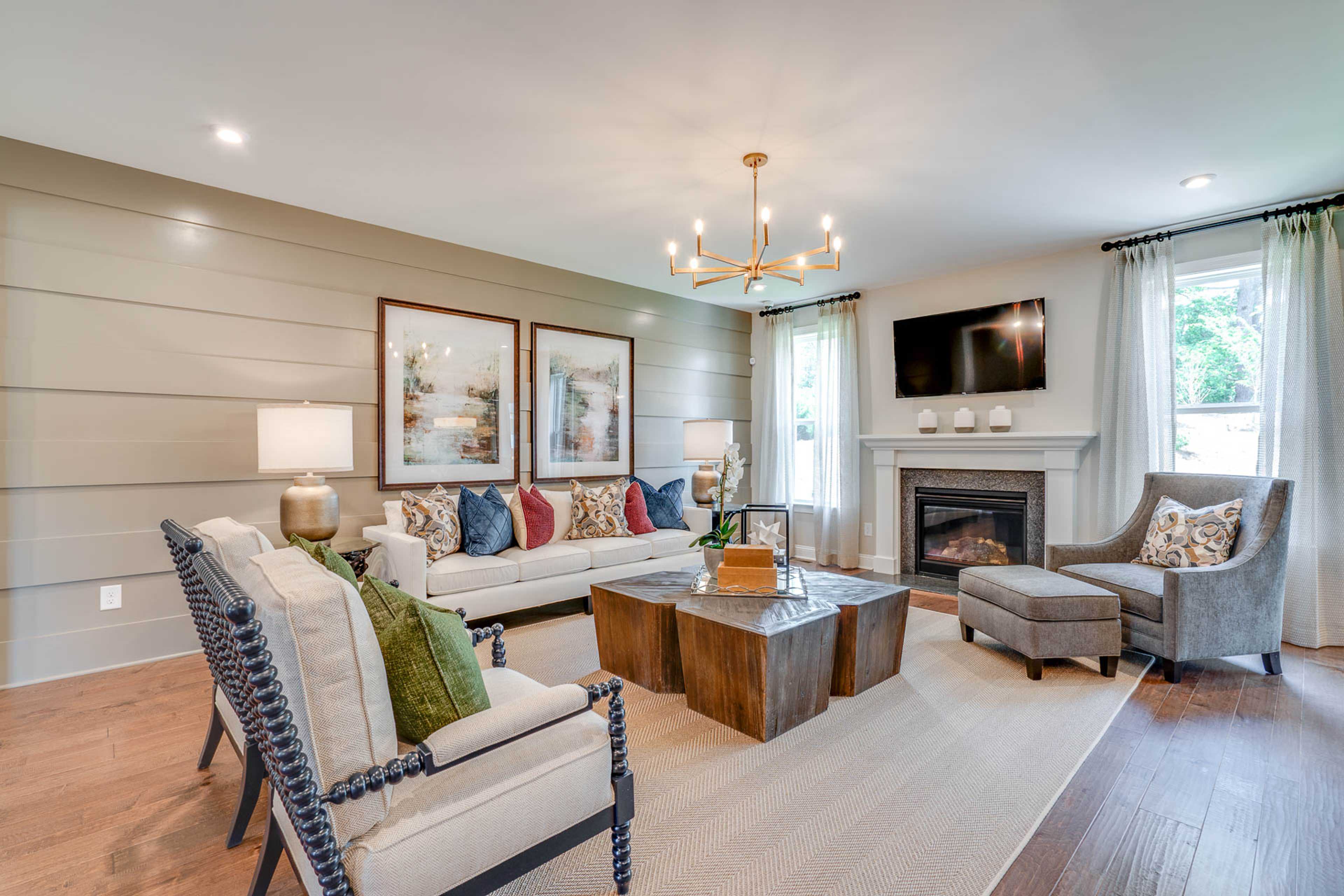 Spacious living room at Hasentree in Wake Forest NC by Davidson Homes featuring gas fireplace, chandelier, plush armchairs, and hardwood floors