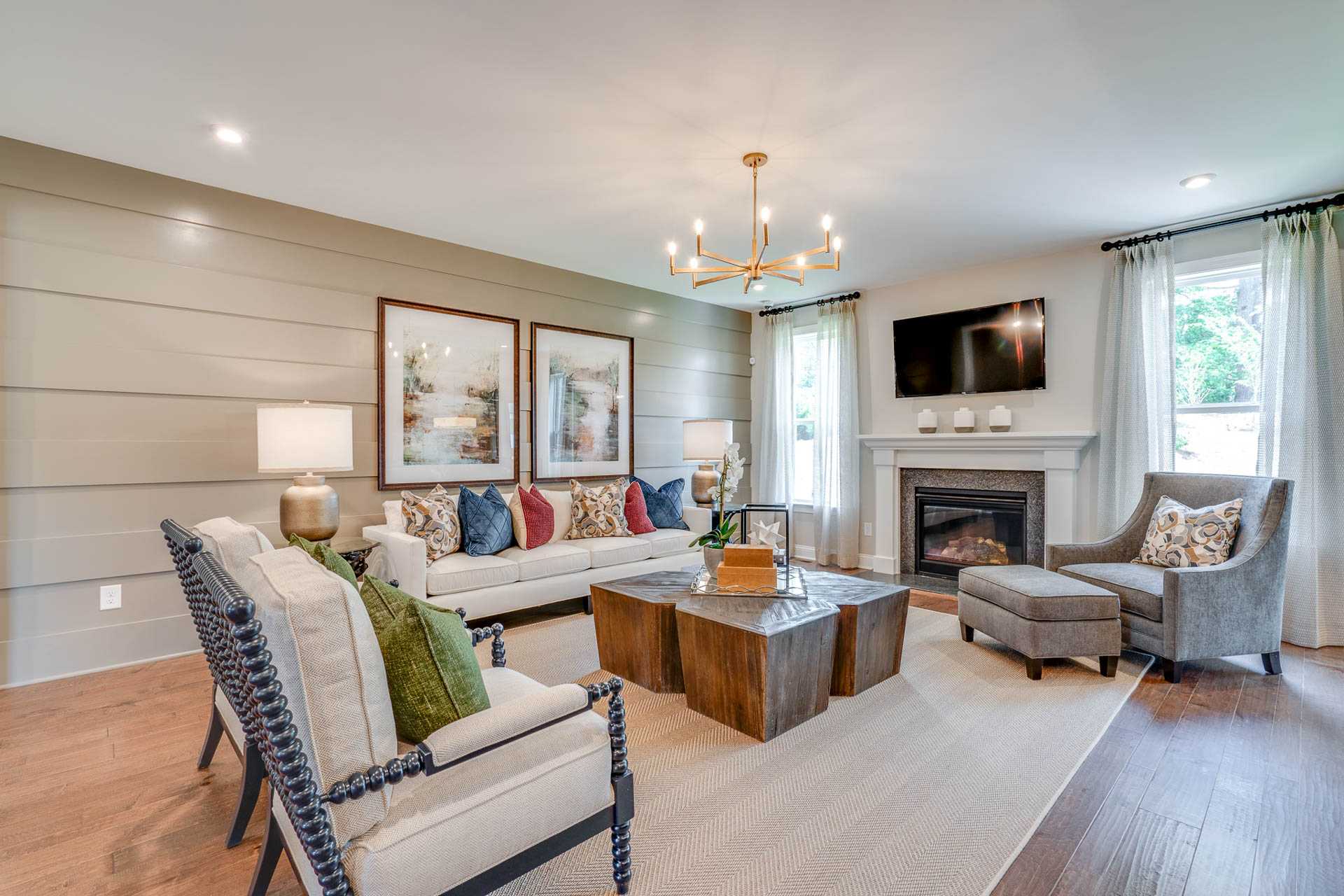 Spacious living room at Hasentree in Wake Forest NC by Davidson Homes featuring gas fireplace, chandelier, plush armchairs, and hardwood floors