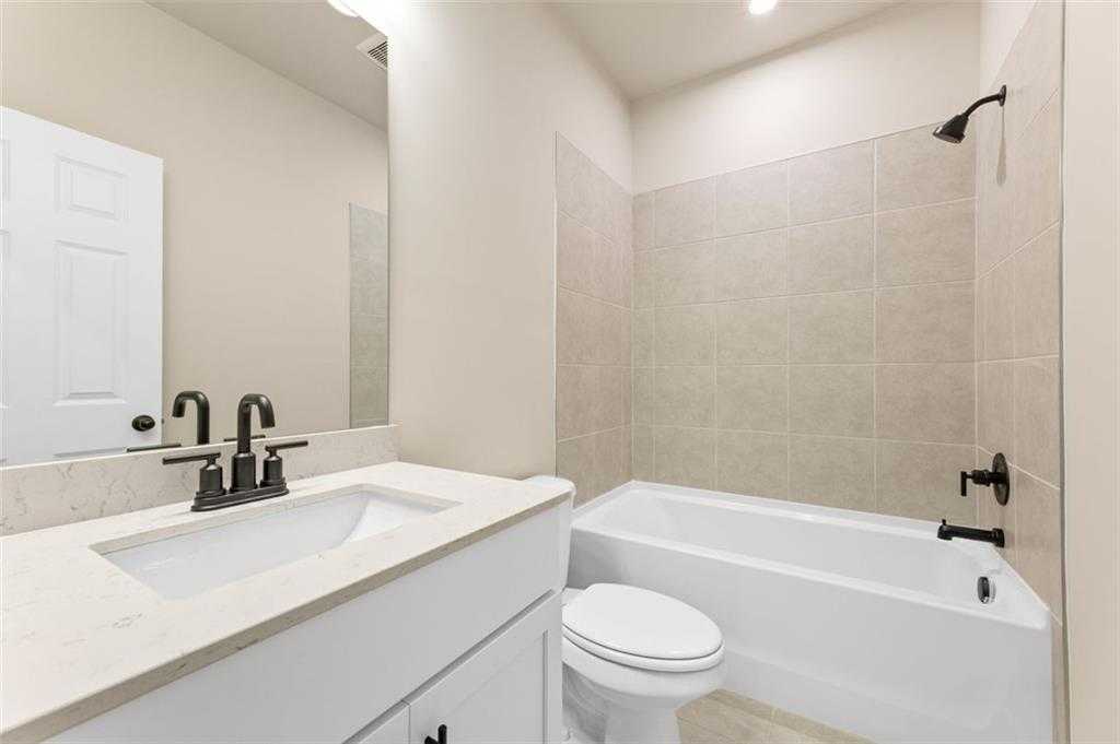 Bright bathroom with tub-shower combo, beige tile surround, quartz vanity, and white fixtures in Davidson Homes The Harrison G, Hoschton, GA