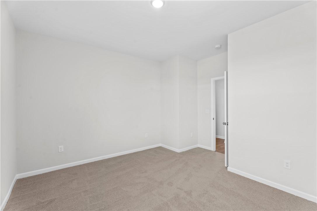 Spacious empty bedroom with beige carpet, white walls, and open door in Davidson Homes The Luna B, Opelika, Alabama