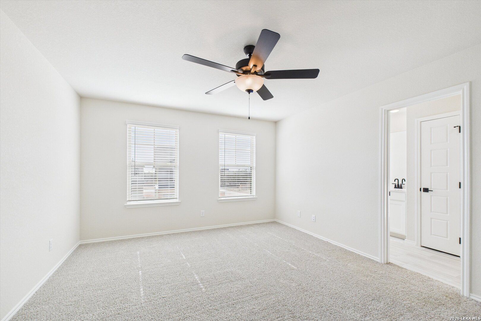 Bright secondary bedroom with beige walls, carpet floor, ceiling fan, and en-suite bath in Davidson Homes The Gillian B, San Antonio