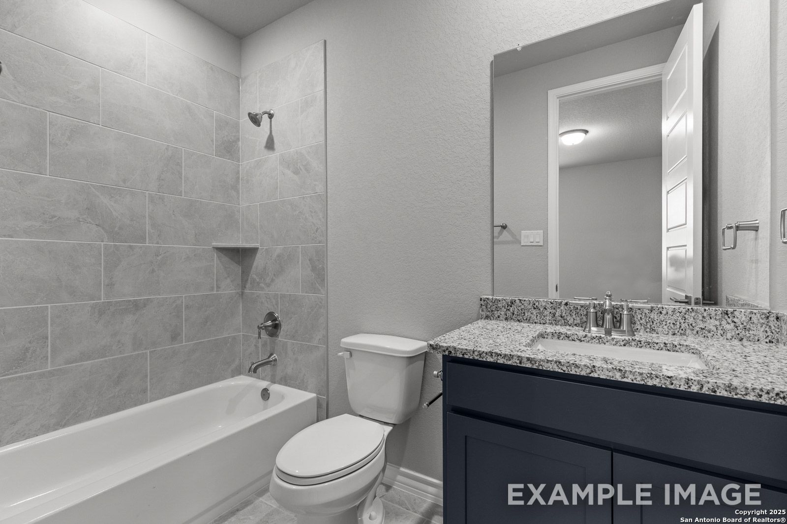 Modern bathroom in The Oxford H featuring a tub-shower combo with gray tile surround and dark vanity with granite countertop.