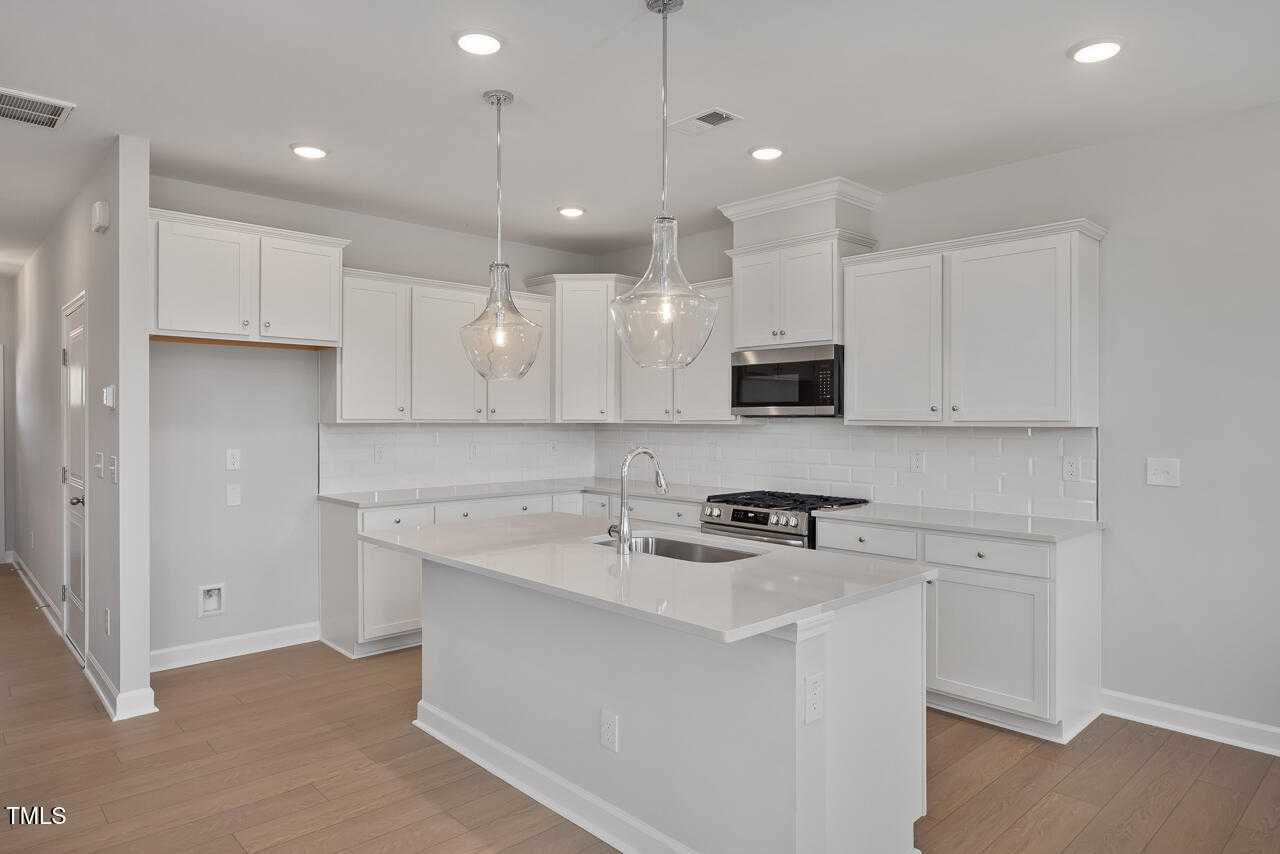 Modern white kitchen with quartz island sink, stainless appliances, shaker cabinets, and pendant lights in Davidson Homes The Graham, Fuquay-Varina, NC