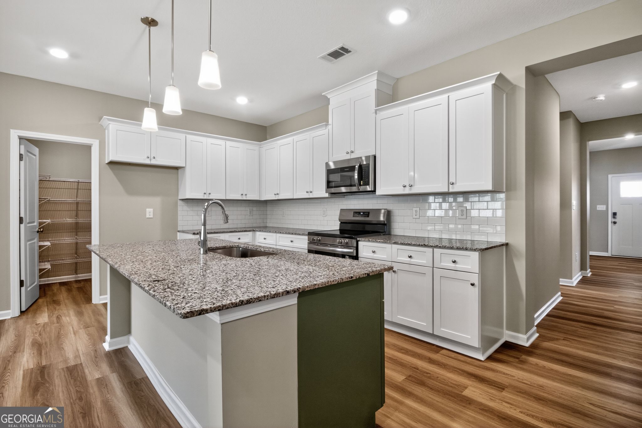 Modern white kitchen with granite island, subway tile backsplash, stainless appliances in The Luna home, Ivy Glen, Perry, GA