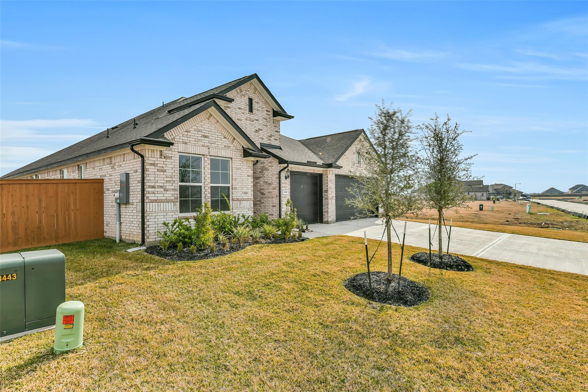 Modern 1-story beige brick home with 3-car garage, landscaped side yard, and young trees in Lago Mar, Texas City - Davidson Homes The George A