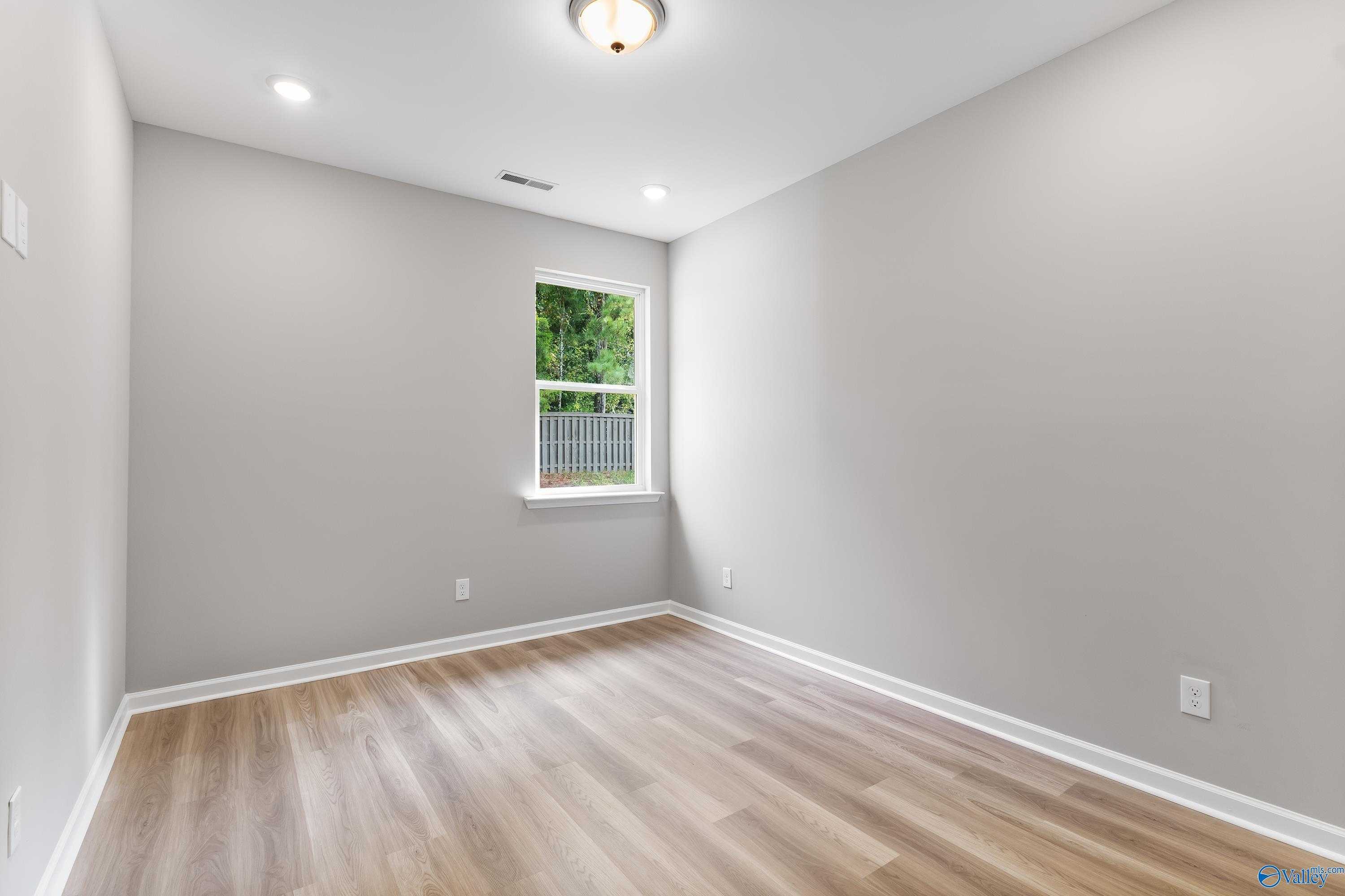 Bright secondary bedroom with gray walls, hardwood floors, and backyard window view in Evermore Homes The Grace, Madison, Alabama