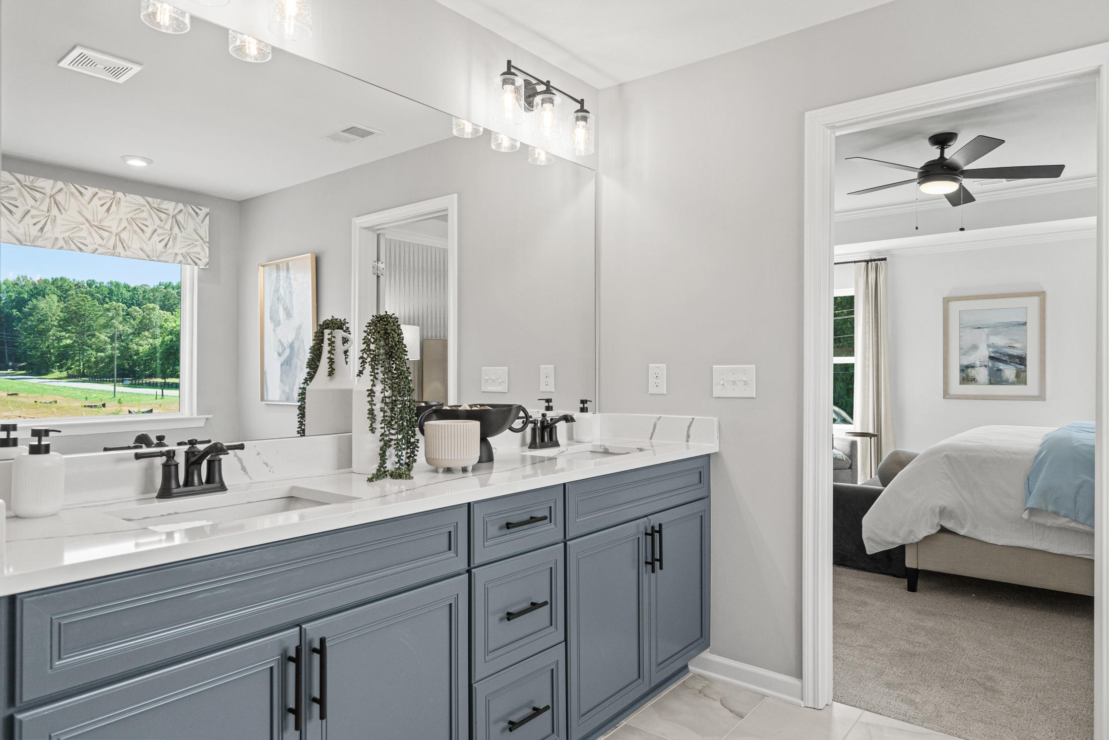 The Hickory B master bathroom with navy blue double vanity, quartz counters, mirrors, plants, and bedroom view
