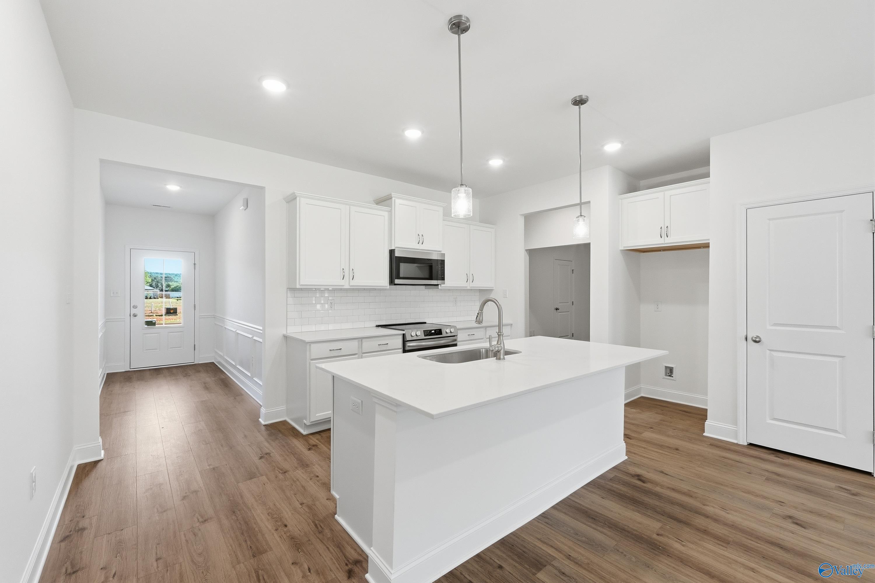 Bright white kitchen with island sink, stainless appliances, subway tile backsplash, and hardwood floors in Davidson Homes The Cumberland D, Decatur AL