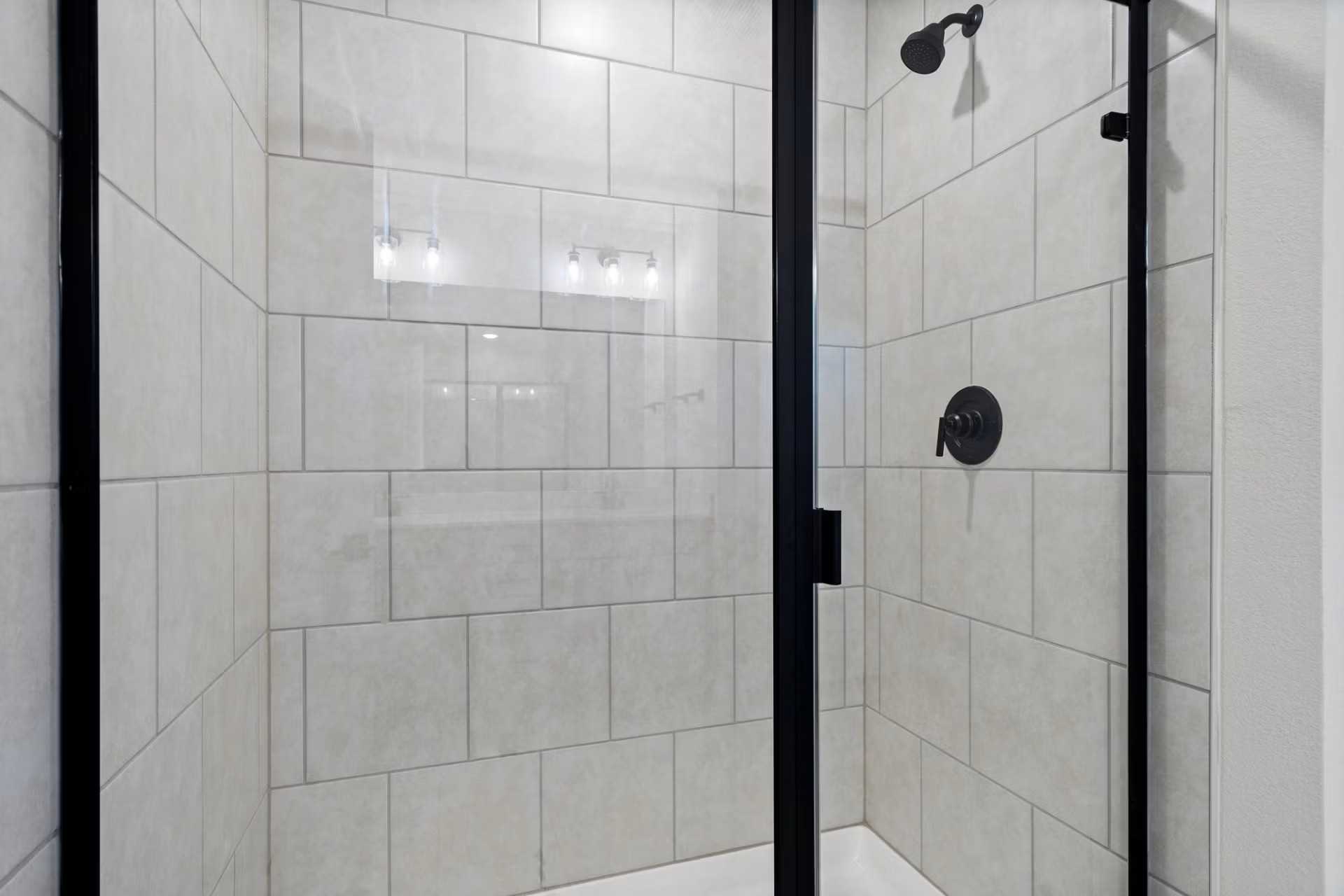 Modern walk-in shower with frameless glass door, white subway tile, and black fixtures in Davidson Homes The Wake D, Wylie, Texas