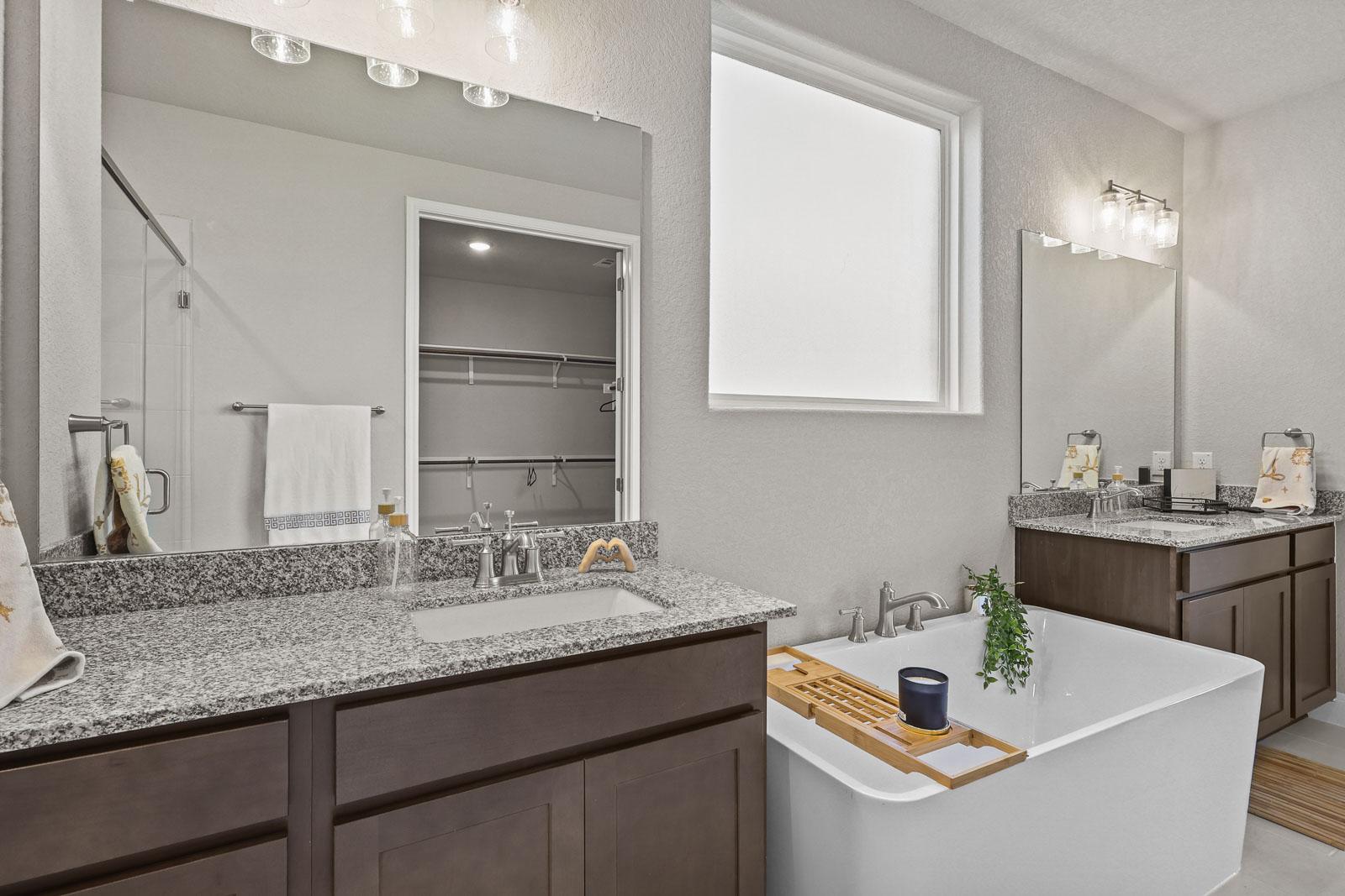 Spacious master bathroom in The Jennings G featuring dual granite vanities, a deep soaking tub, and walk-in closet access.