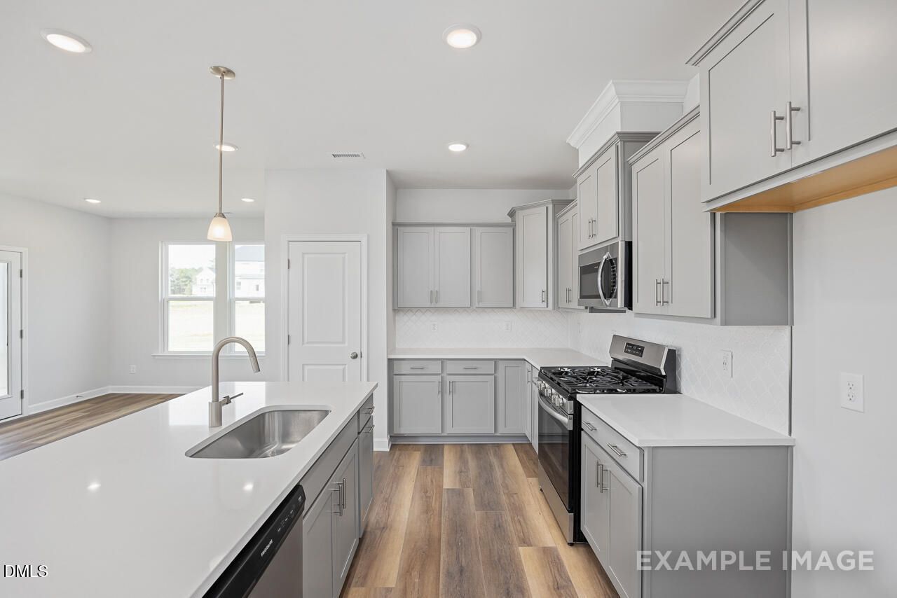 Modern open-concept kitchen featuring white shaker cabinets, stainless steel appliances, quartz island, and LVP flooring in The Daphne C, Lillington, NC