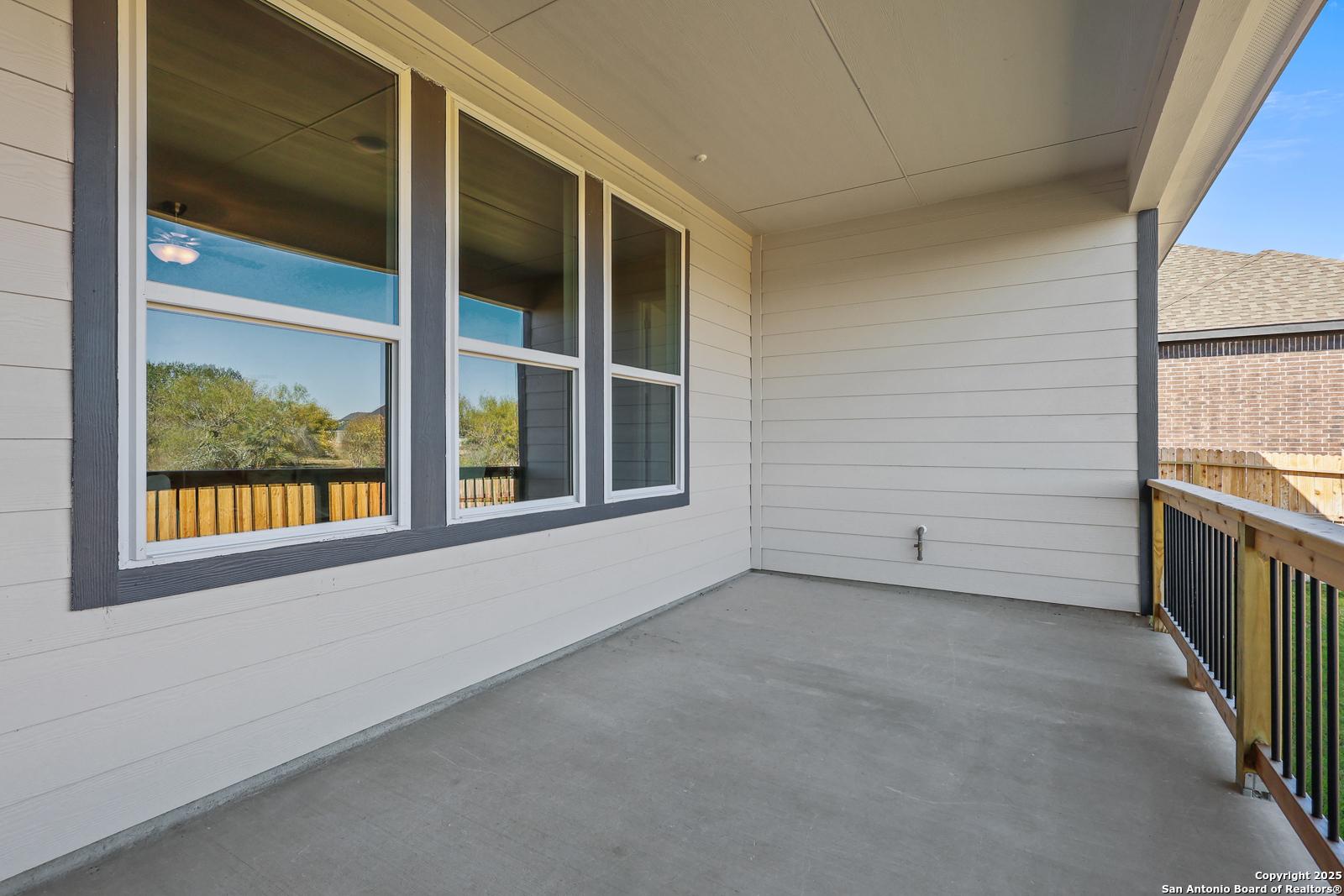 Covered balcony with large sliding windows, wooden railing, and tree views in Davidson Homes The Jennings G, Castroville, Texas