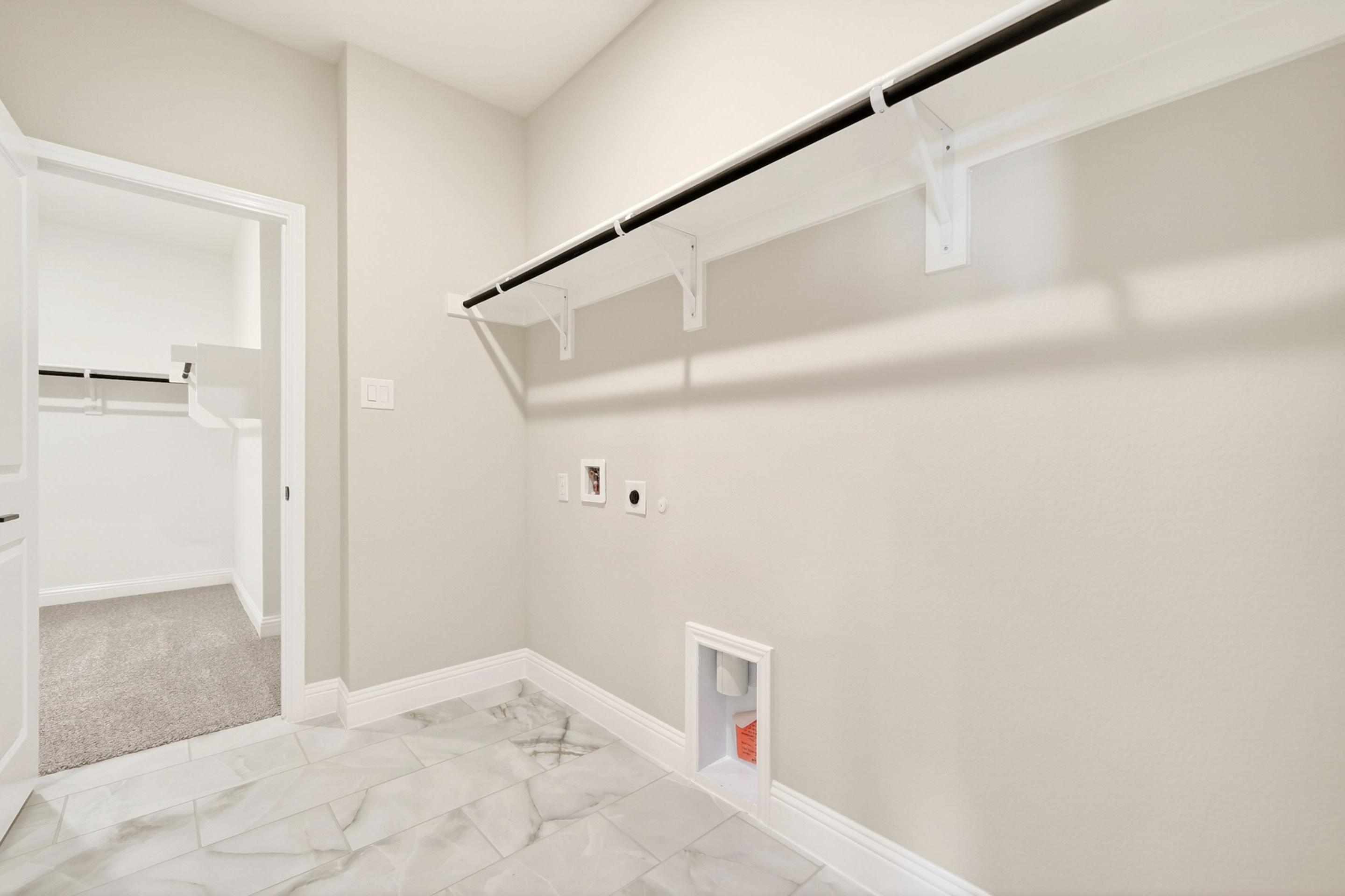 Spacious laundry room in The Holly design featuring tiled floors, utility hookups, and built-in shelving.