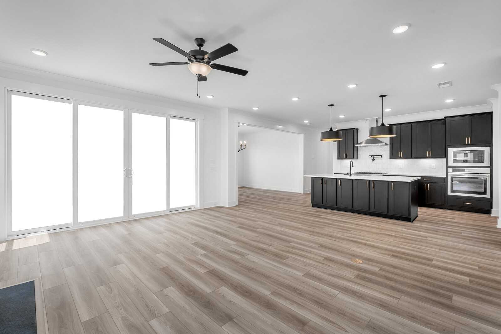 Open-concept living room and kitchen with dark cabinetry, center island, ceiling fan, and large sliding doors in Davidson Homes The Hathaway, Murfreesboro TN