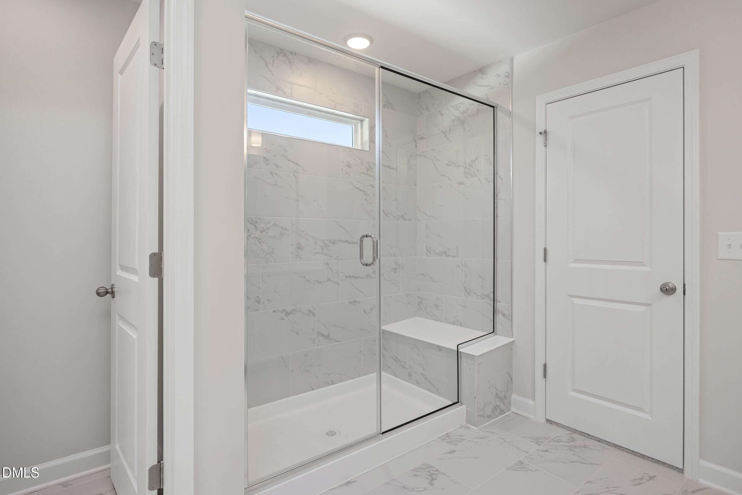 Modern frameless glass shower with white marble tiles, bench seat, and clerestory window in master bath of Davidson Homes The Preston C in Lillington, NC