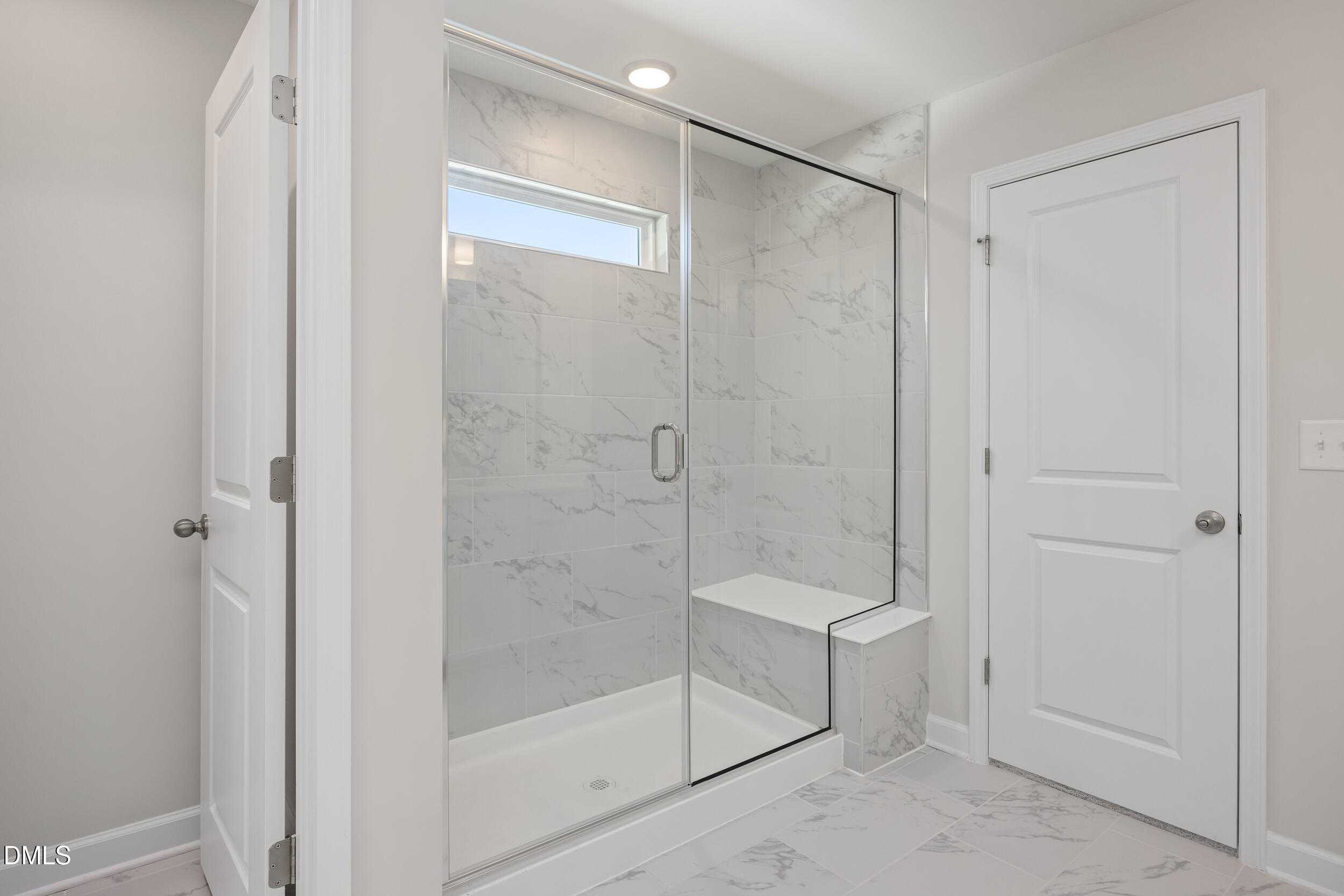 Modern frameless glass shower with white marble tiles, bench seat, and clerestory window in master bath of Davidson Homes The Preston C in Lillington, NC