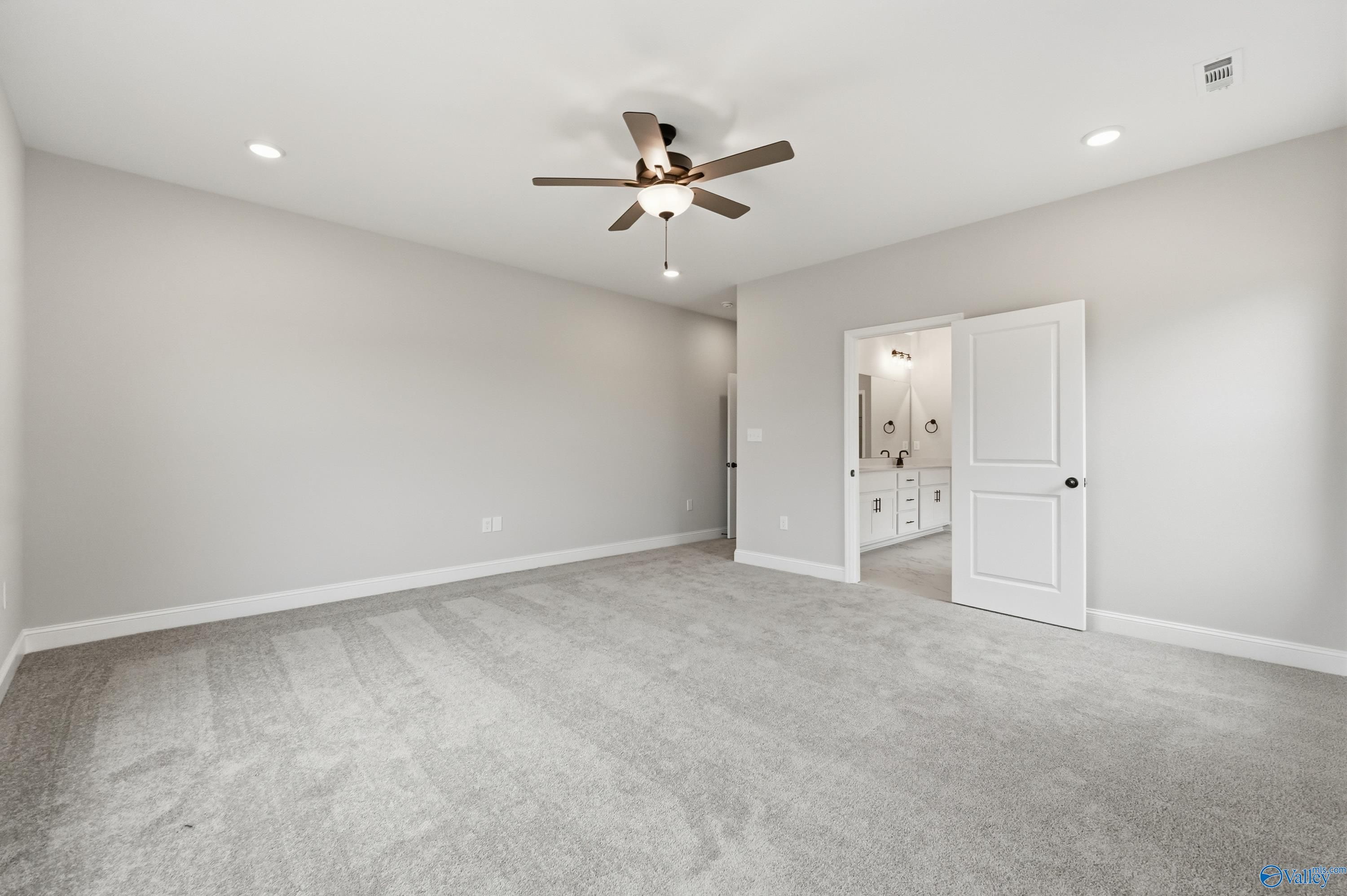 Spacious bedroom with ceiling fan, gray walls, and open door to bathroom with double vanity in Davidson Homes The Finleigh, Meridianville, Alabama