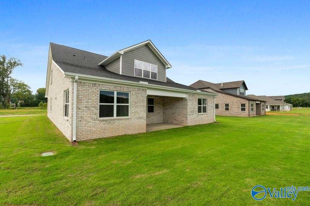 1.5-story brick home with gray siding, covered patio, and lush green lawn in The Meadows at Hampton Cove, Owens Cross Roads, Alabama
