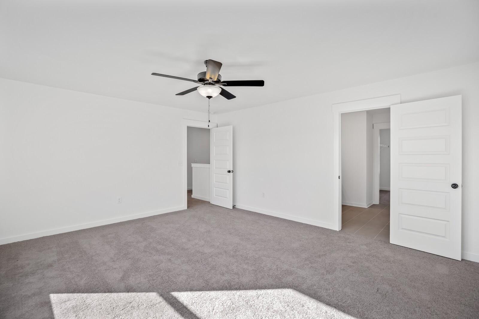 Spacious secondary bedroom featuring ceiling fan, open closet doors, and beige carpet in Davidson Homes The Willow C, Gallatin, TN