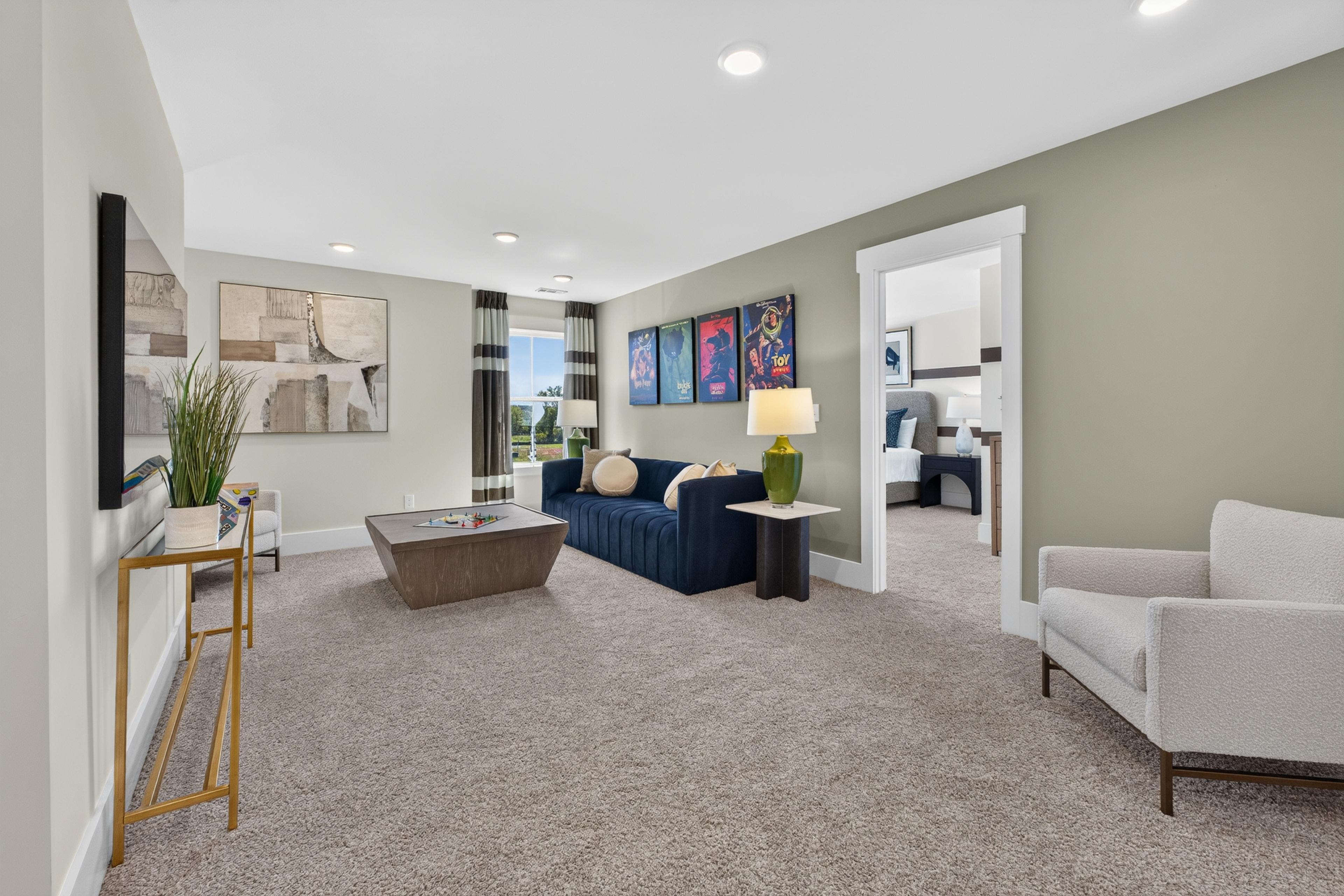 Spacious bonus room with navy sofa and plush carpet at Evergreen Mill by Davidson Homes in Madison, Alabama