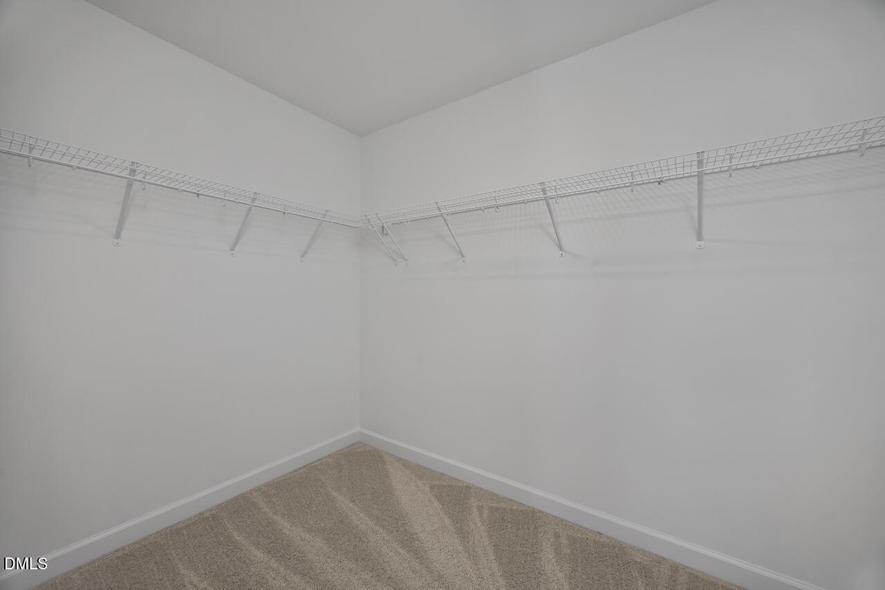 Walk-in closet with white wire shelving and plush carpeting in The Graham floor plan at Springvale, Fuquay-Varina, NC.