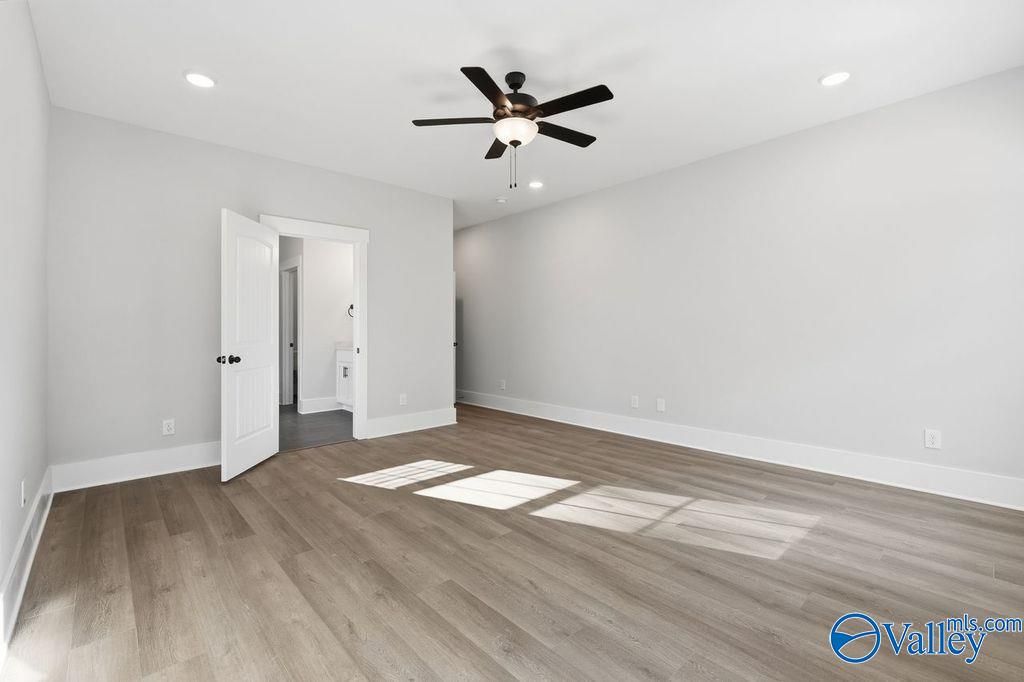 Spacious bedroom with ceiling fan, light hardwood floors, and open en-suite bathroom door in Davidson Homes The Rockford, Hartselle, Alabama