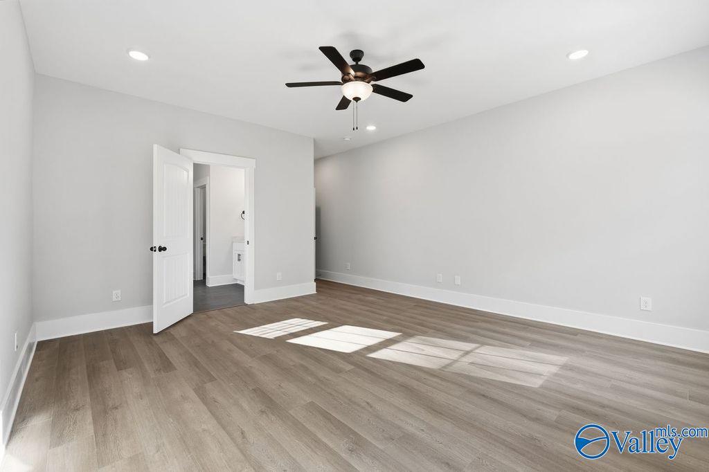 Spacious bedroom with ceiling fan, light hardwood floors, and open en-suite bathroom door in Davidson Homes The Rockford, Hartselle, Alabama