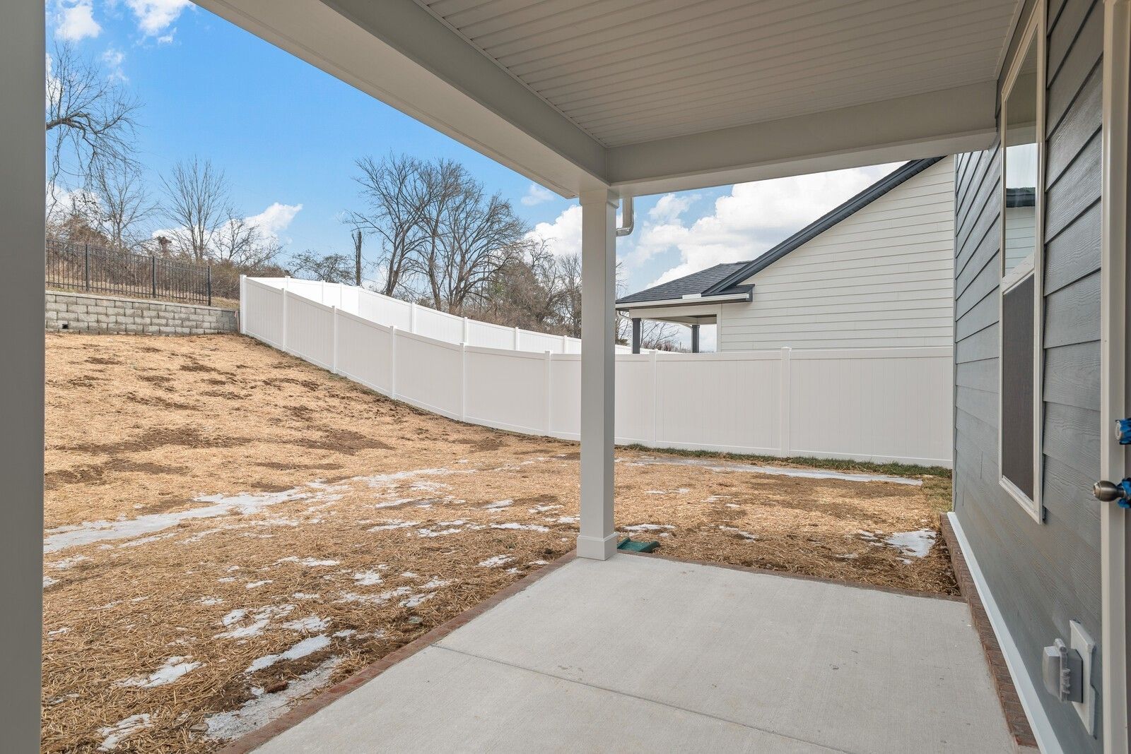 Covered concrete patio with white vinyl fence and wooded hillside view in Davidson Homes The Logan C, Gallatin, Tennessee