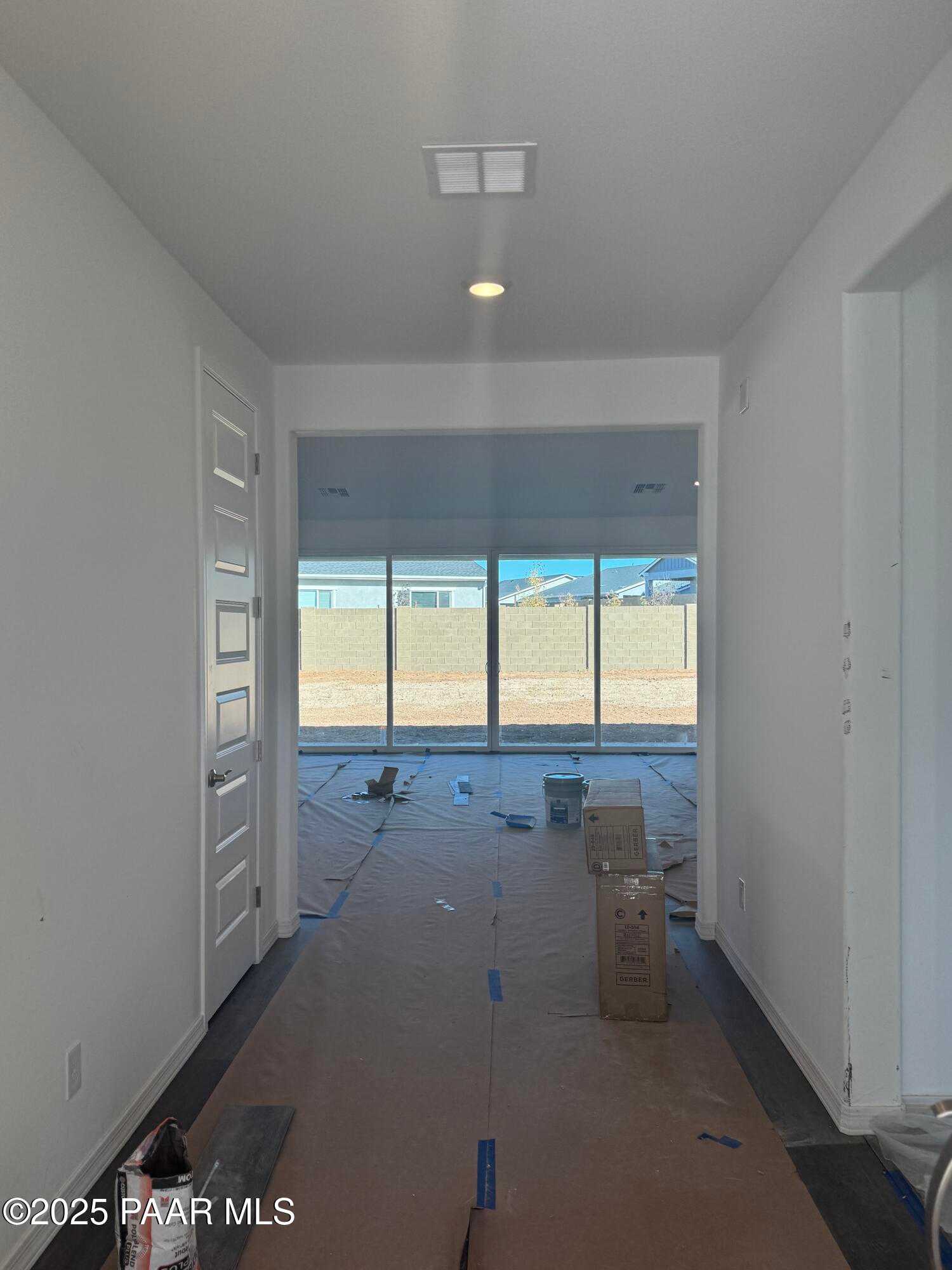 Bright hallway with white walls, open doors, and protective cardboard flooring leading to backyard view through large windows in Davidson Homes The Summit A, Prescott, Arizona