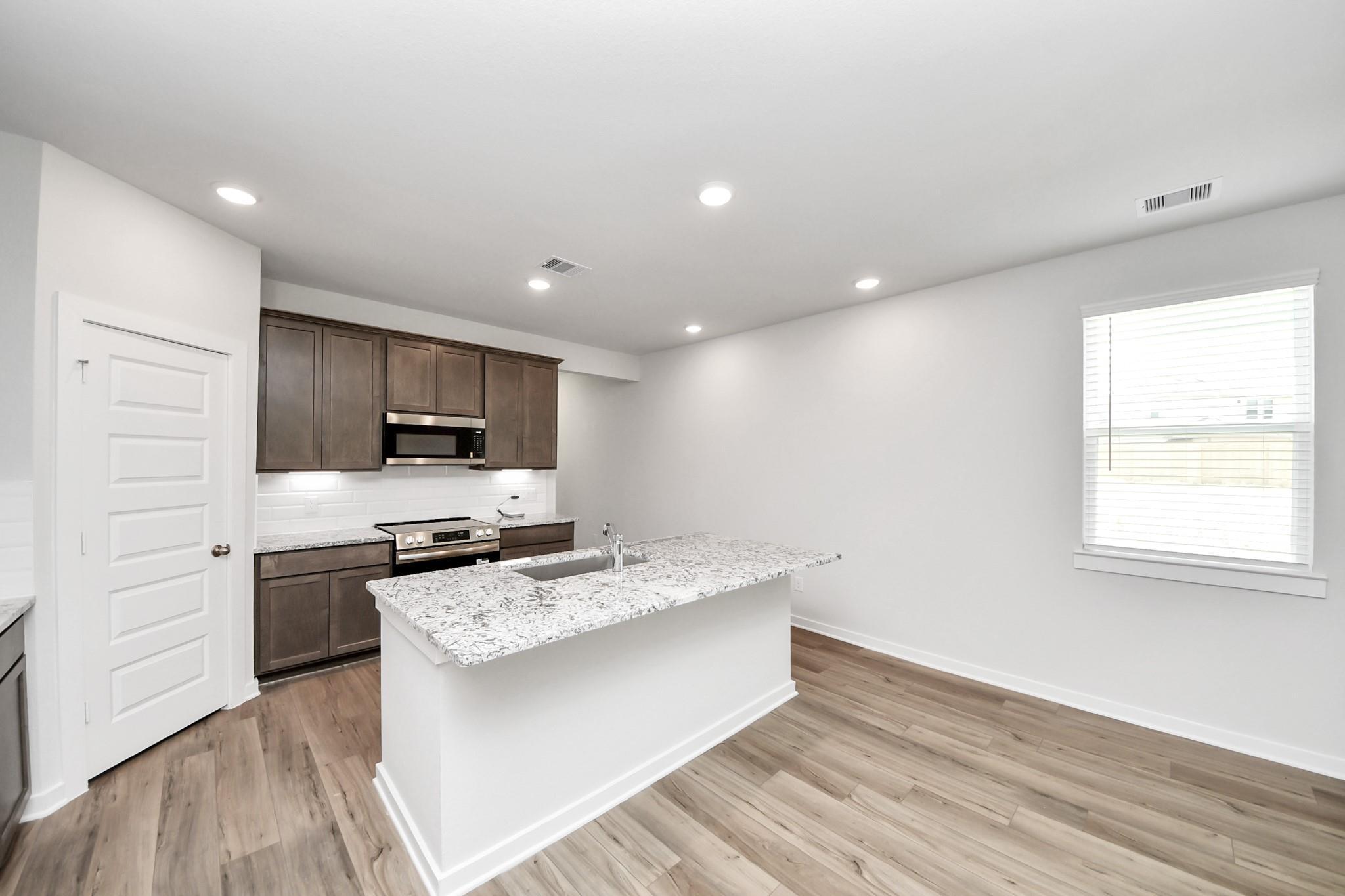 Modern kitchen with granite island and dark wood cabinets in The Sabine E floor plan at Liberty Estates, Cleveland, Texas.