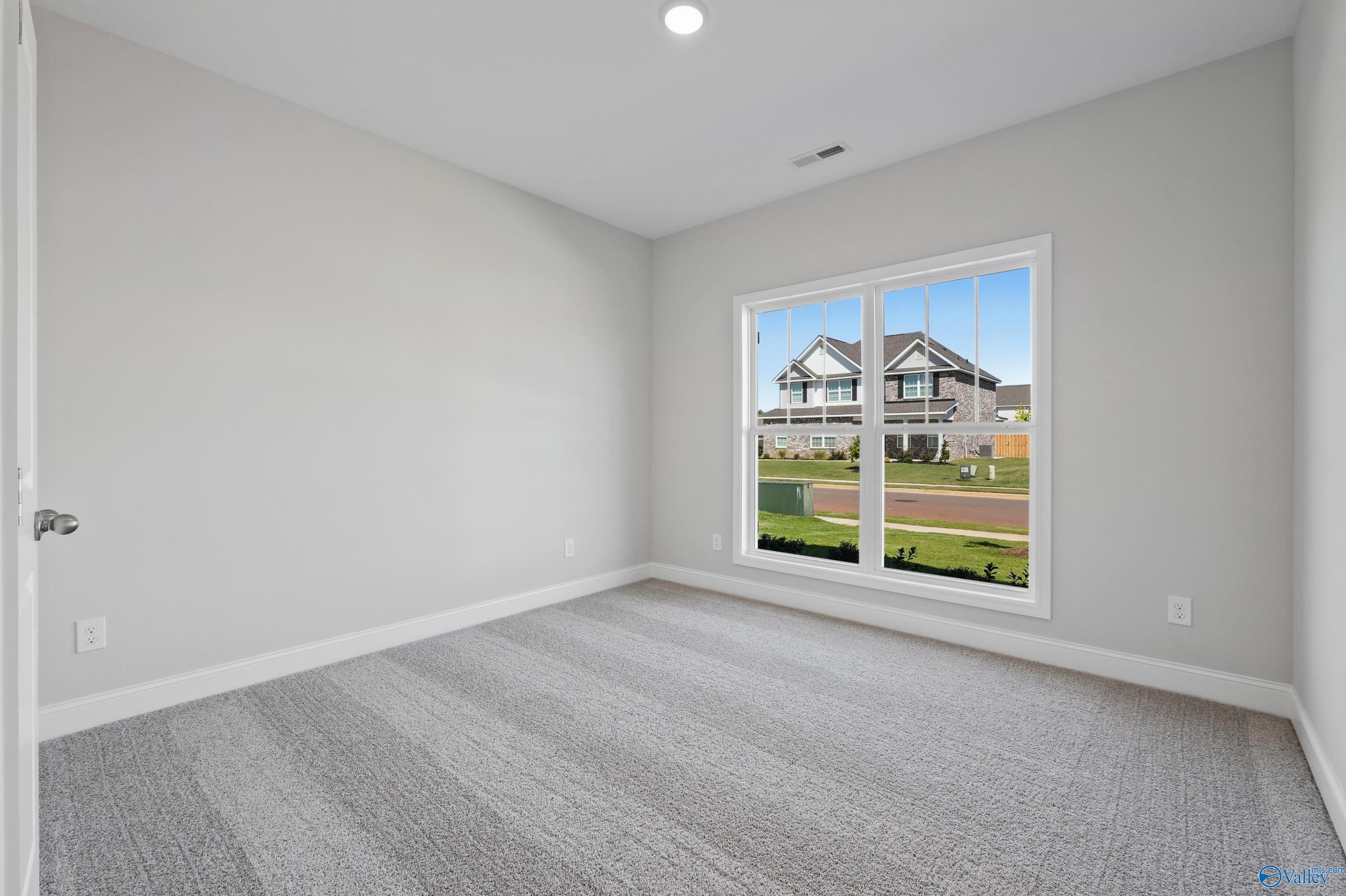 Empty bedroom with gray walls, carpeted floor, and large window view of suburban homes in Davidson Homes The Everett, Hazel Green, Alabama