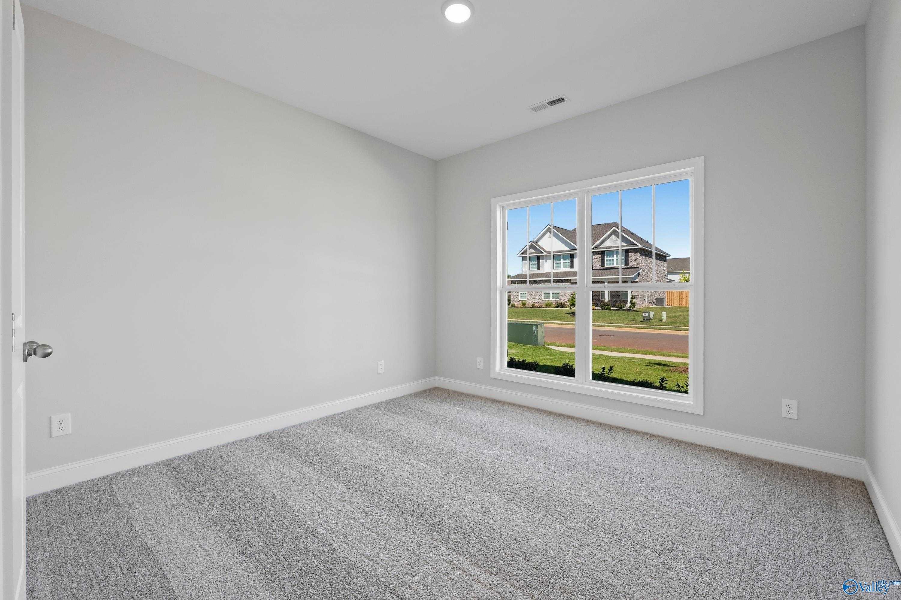 Empty bedroom with gray walls, carpeted floor, and large window view of suburban homes in Davidson Homes The Everett, Hazel Green, Alabama