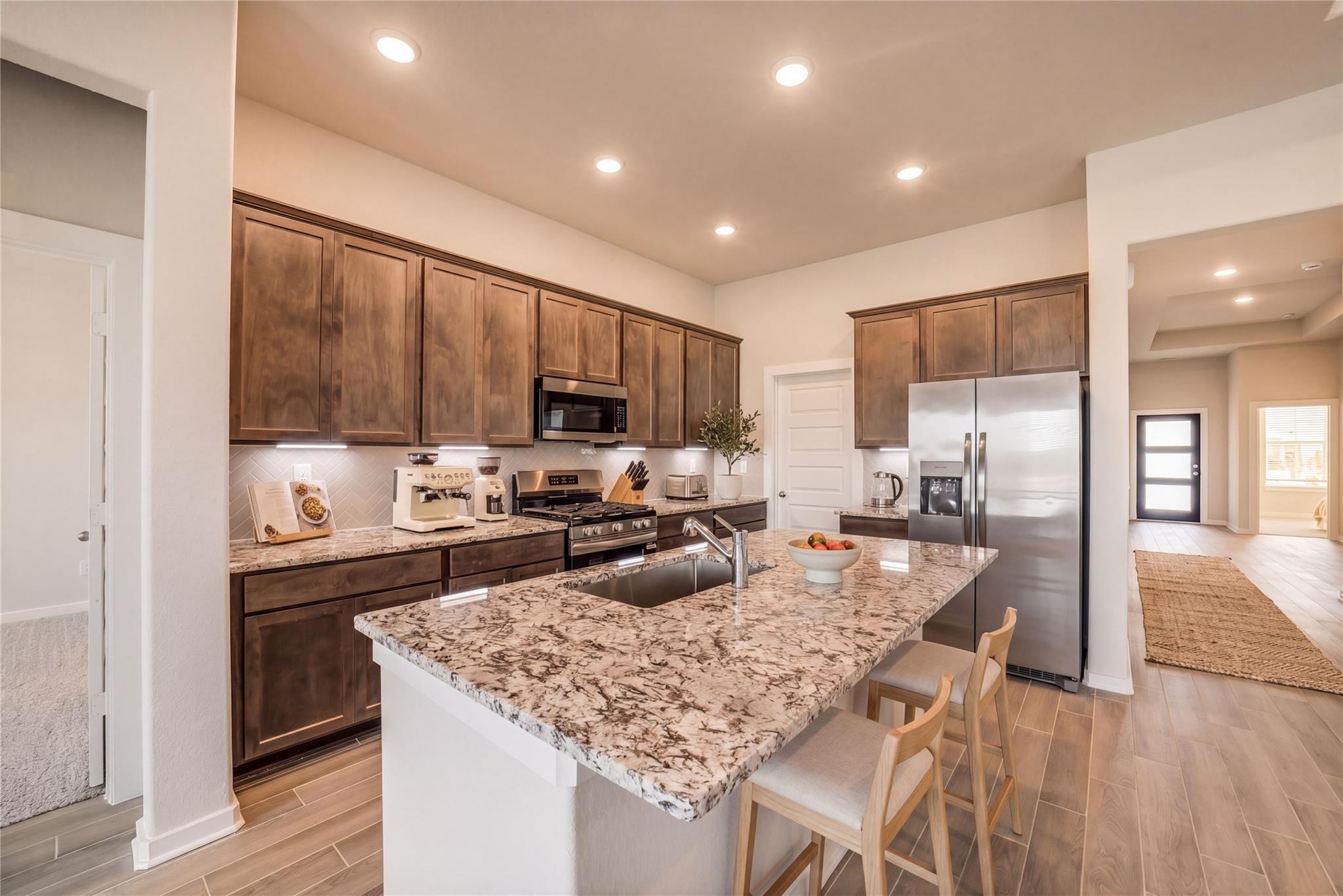 Open-concept kitchen with granite countertops, stainless appliances, shaker cabinets in Davidson Homes Acadia C, Magnolia TX