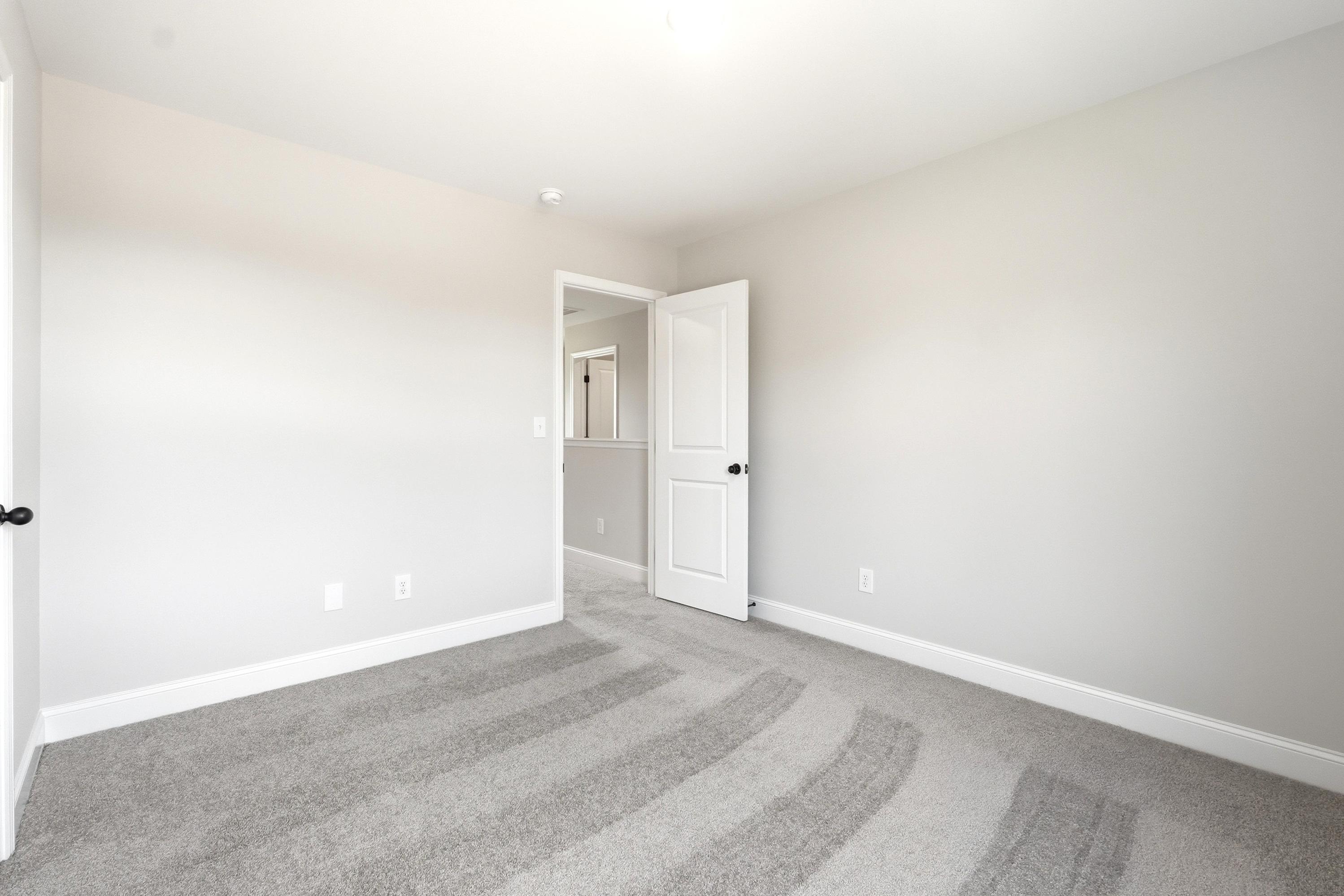 Spacious secondary bedroom in The Russell A floor plan featuring neutral paint, plush carpeting, and an open doorway.