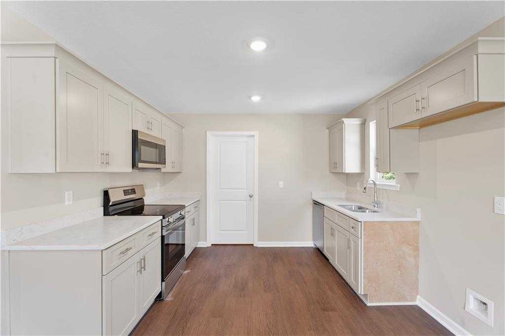 Modern white shaker kitchen with stainless steel appliances, quartz counters, and hardwood floors in Davidson Homes The Washington, Phenix City, Alabama