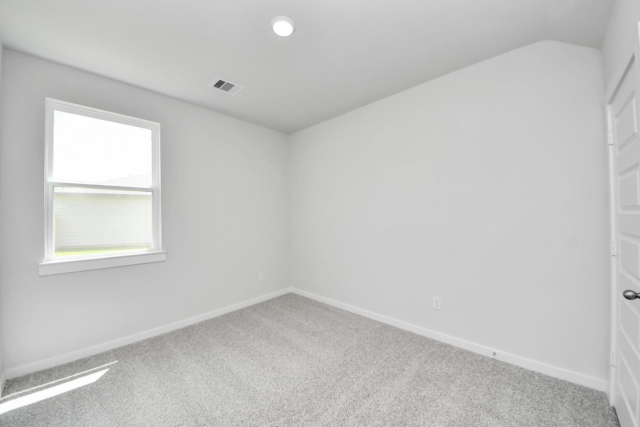 Bright bedroom with neutral carpet and window in The Sabine F floor plan at Liberty Estates, Cleveland, Texas.