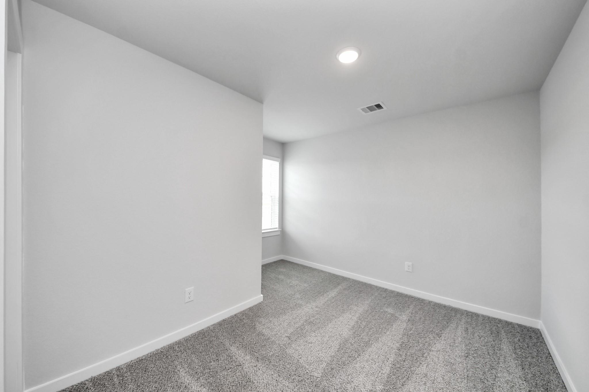 Bright, carpeted spare bedroom in The Sabine E floor plan at Liberty Estates, Cleveland, Texas.