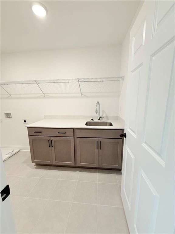 Laundry room with utility sink, white countertops, and storage cabinets in The Hickory B home at Wehunt Meadows, Hoschton.