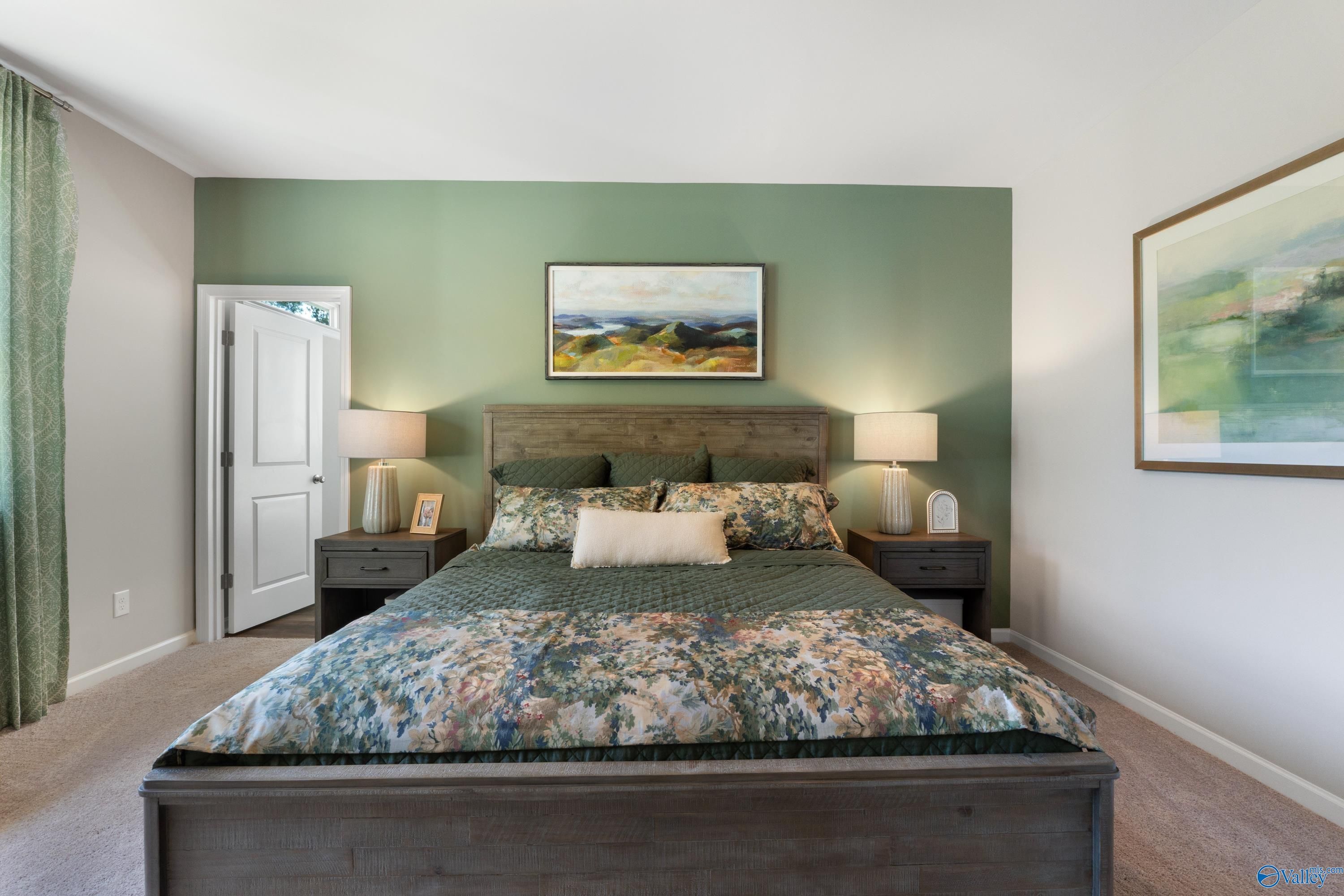 Elegant master bedroom with sage green accent wall, wooden platform bed, floral bedding in Davidson Homes The Stella, Madison AL